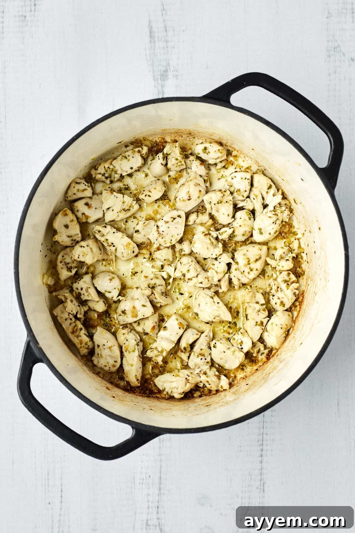 Cooked, seasoned chicken pieces searing in a large pot, ready to be combined with other ingredients for the creamy pasta.