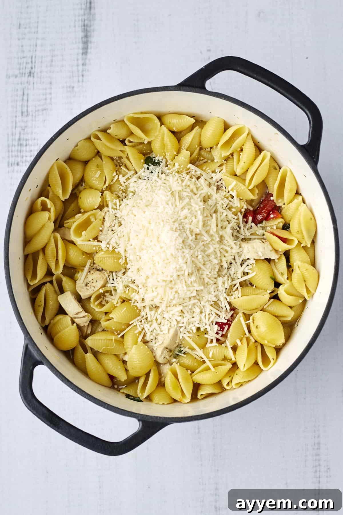 A close-up of freshly grated Parmesan cheese being sprinkled over a bubbling pot of creamy Tuscan chicken pasta, enhancing its rich appeal.