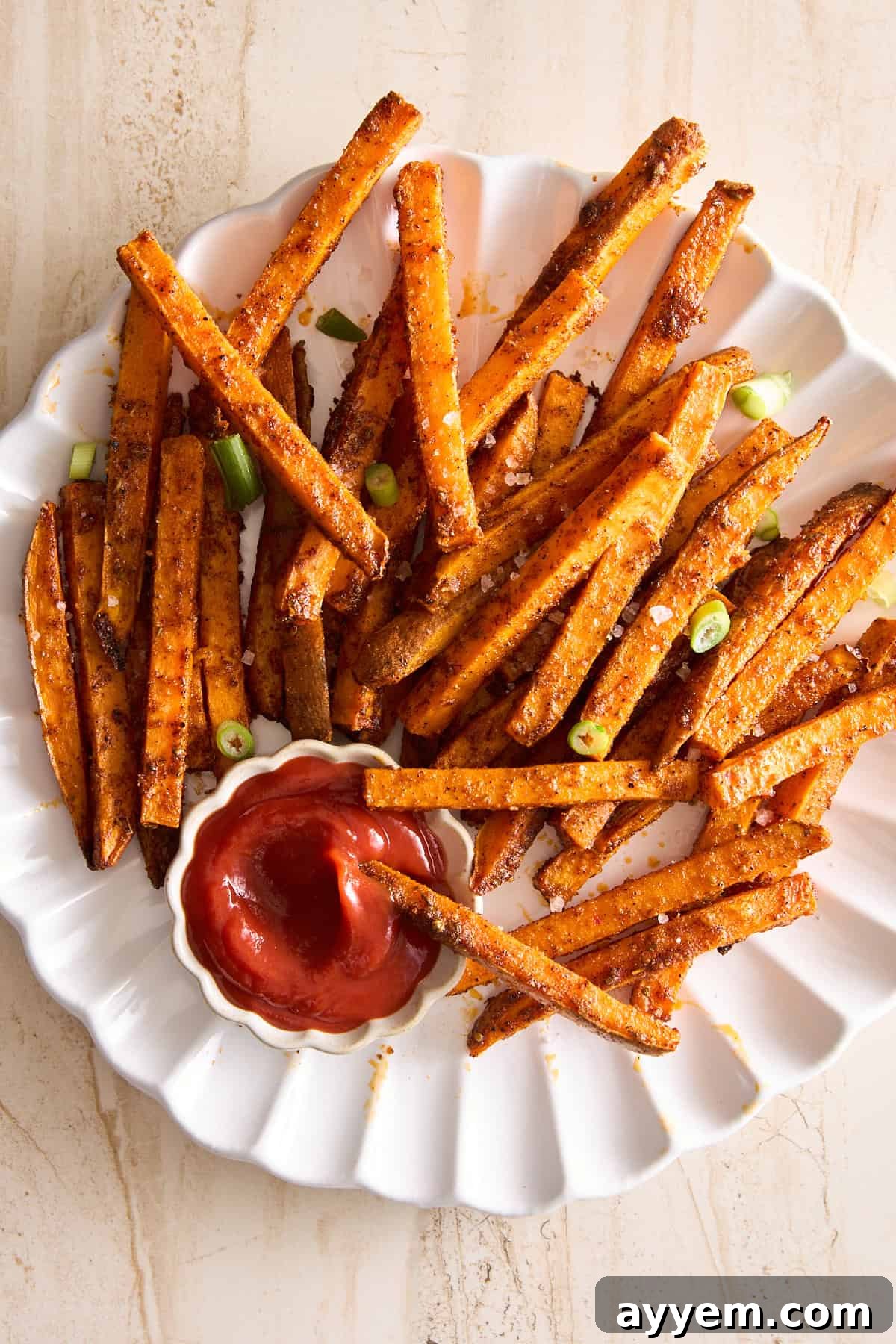A vibrant plate of crispy oven baked sweet potato fries, seasoned to perfection and served with a side of ketchup for dipping.