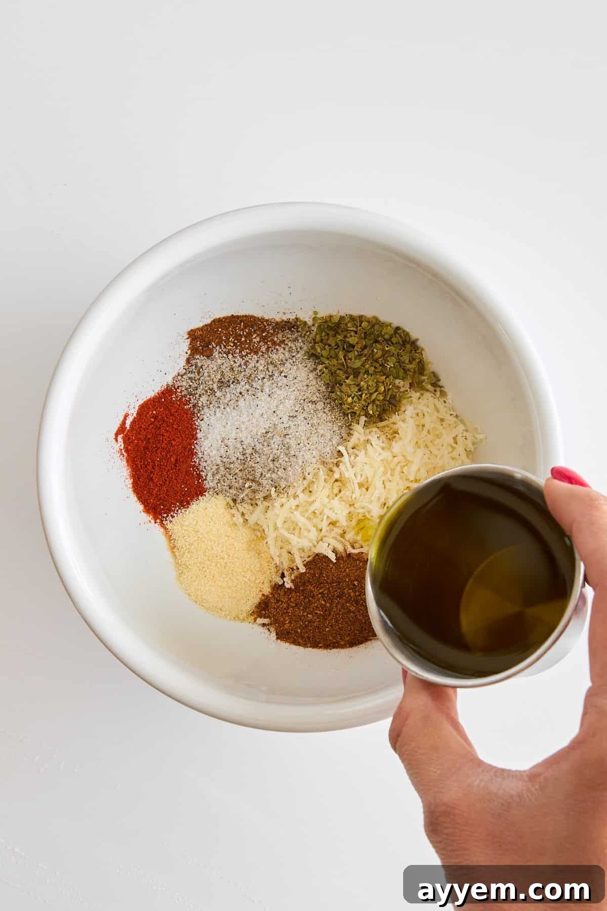 A close-up of the seasoning blend ingredients—chili powder, chipotle, smoked paprika, oregano, garlic powder, and sea salt—mixed together in a bowl, with a hand drizzling olive oil over them.