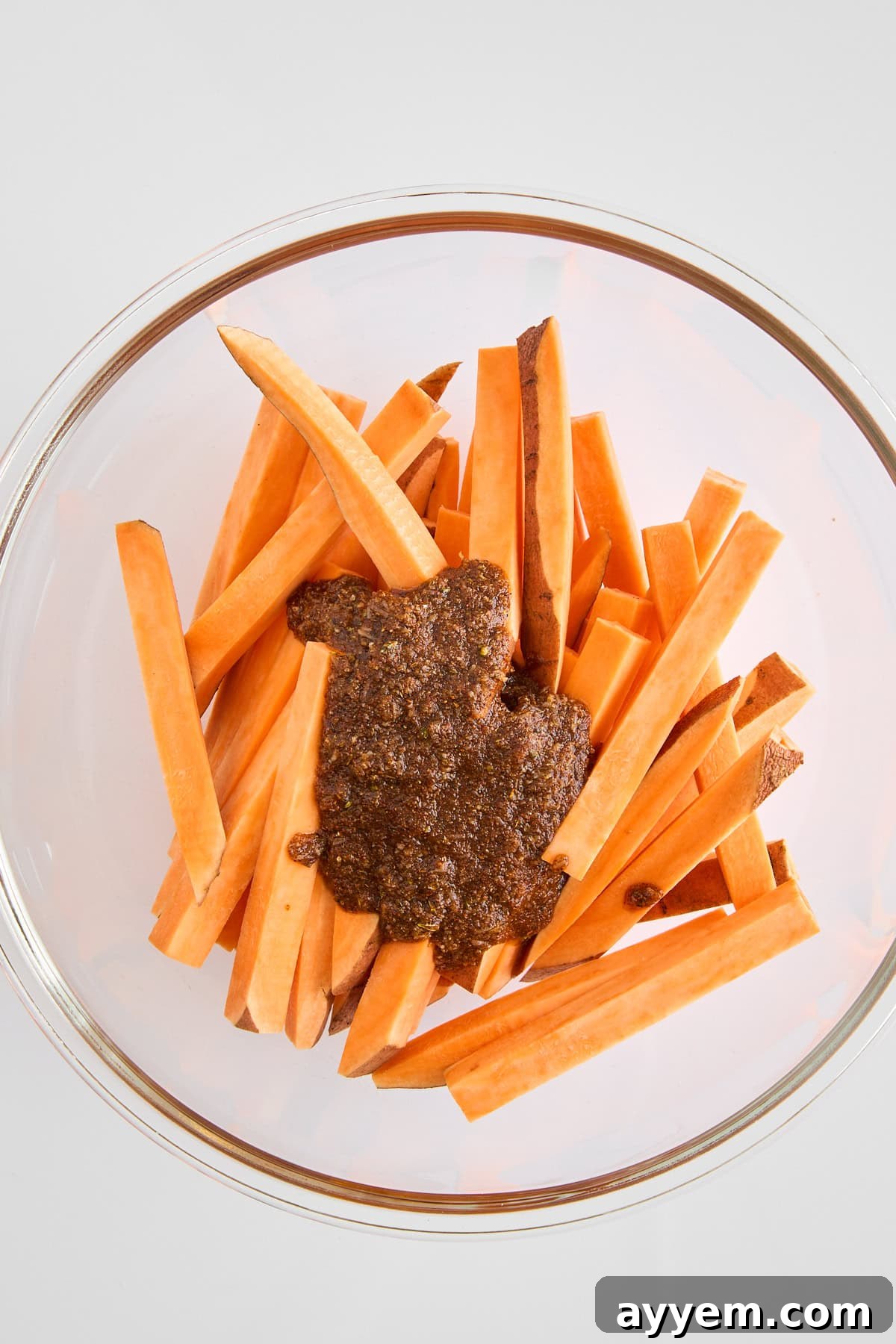 A bowl of raw sweet potato fries, perfectly sliced and coated with a vibrant seasoning mix, ready for baking.