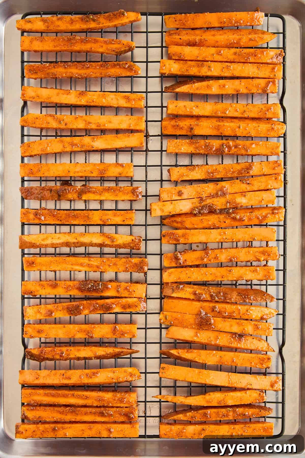 Seasoned sweet potato fries evenly spread in a single layer on a wire rack over a baking sheet, optimized for air circulation and crispiness.