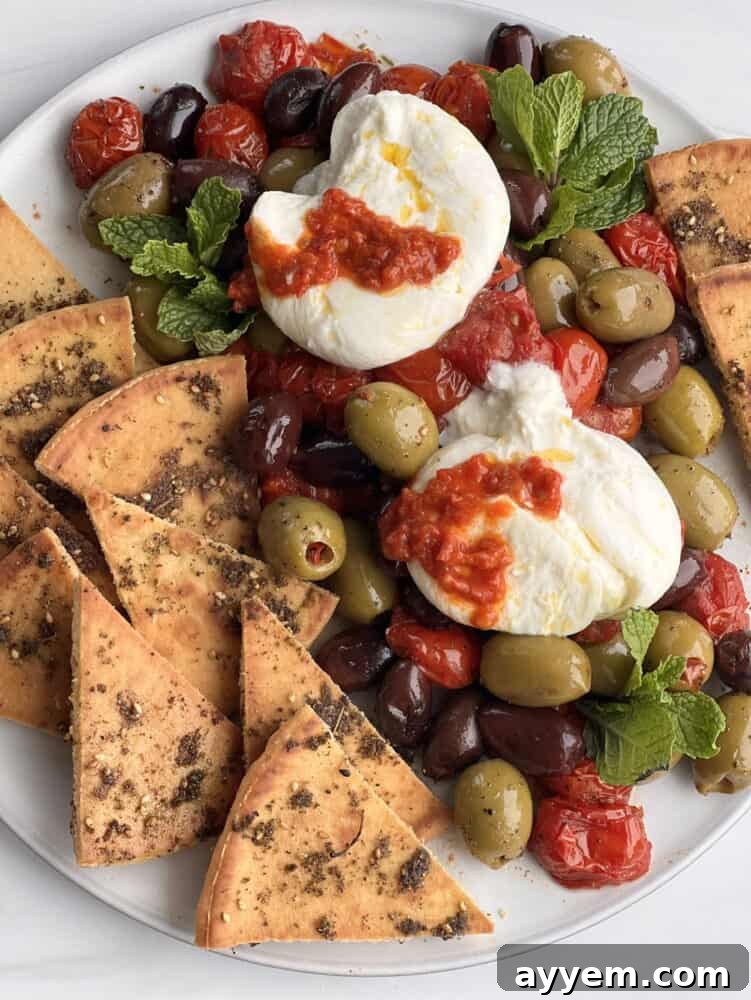 close up view of creamy burrata with roasted tomatoes, olives and zaatar pita on a rustic plate