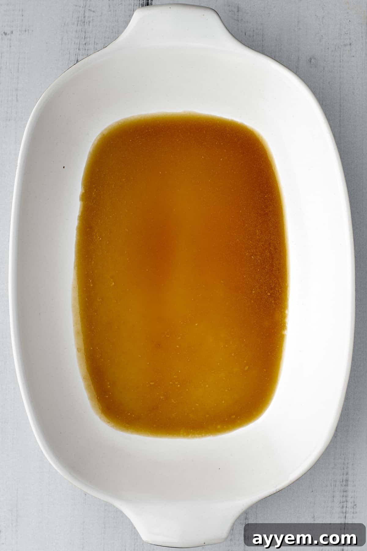 A pool of rich, golden caramel sauce glistening at the bottom of a white ceramic baking dish, ready for cinnamon rolls.