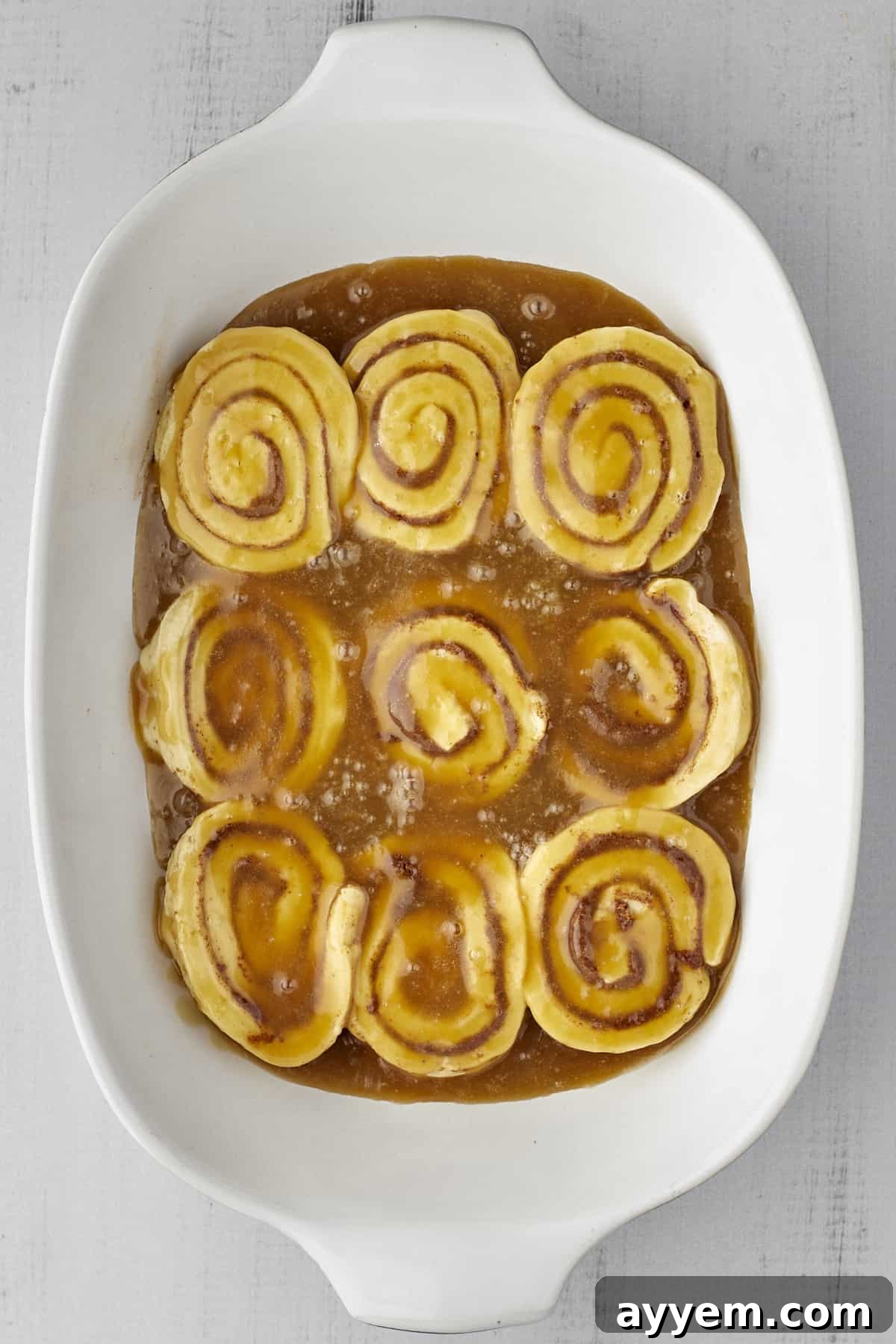 Close-up of unbaked cinnamon rolls nestled between layers of luscious caramel sauce, ready for the final toppings.