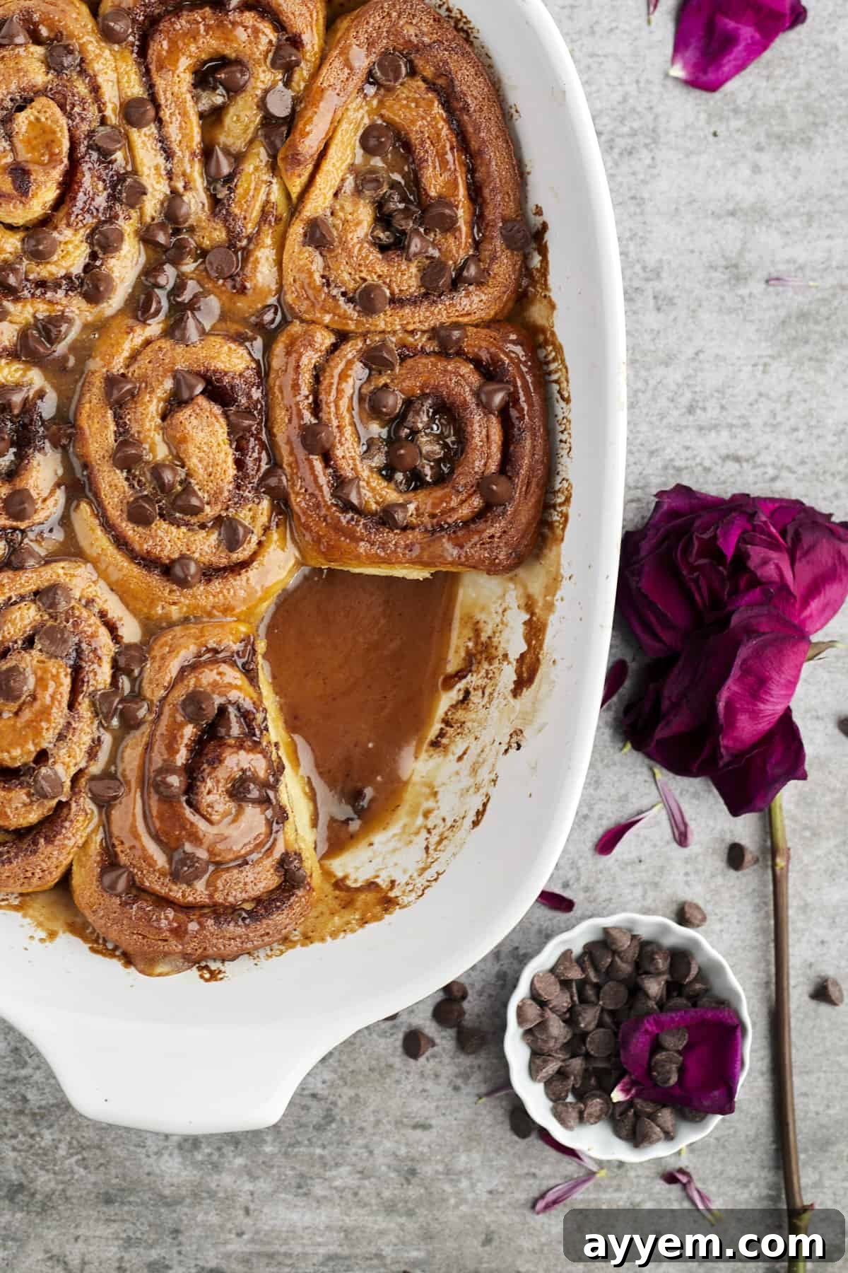 A baking dish of warm, freshly baked caramel chocolate chip cinnamon rolls, with one roll enticingly removed, showing its gooey center.