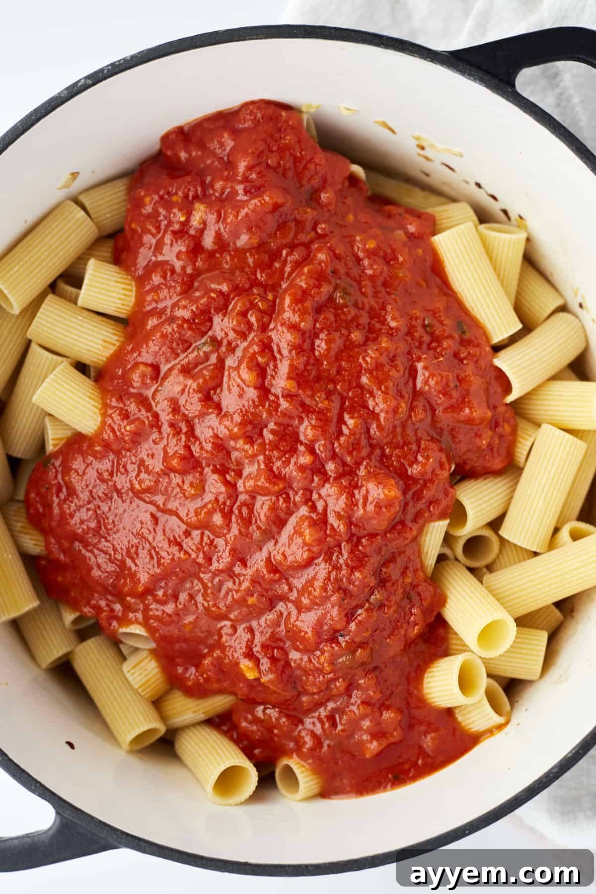 Uncooked rigatoni noodles in a pot, topped with marinara sauce and broth before cooking