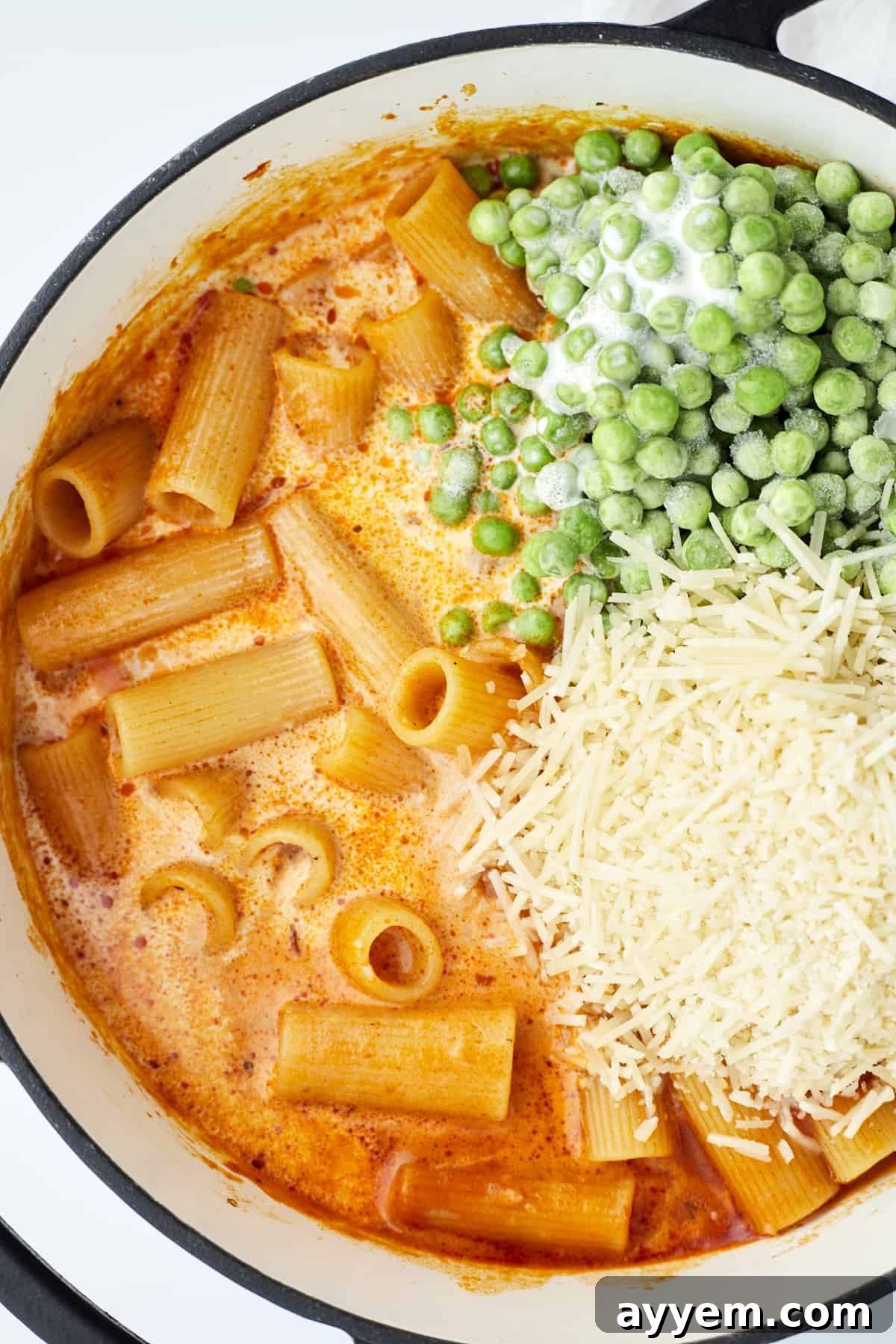 One pot spicy rigatoni in a pot, topped with vibrant green peas and freshly grated Parmesan cheese