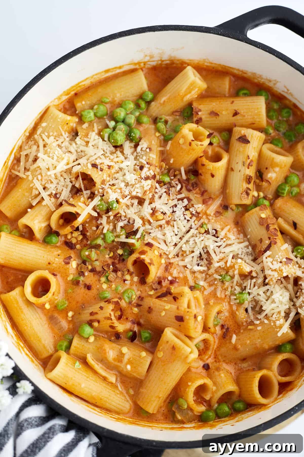 Overhead image of a pot of spicy rigatoni with peas, generously topped with shredded Parmesan and fresh herbs