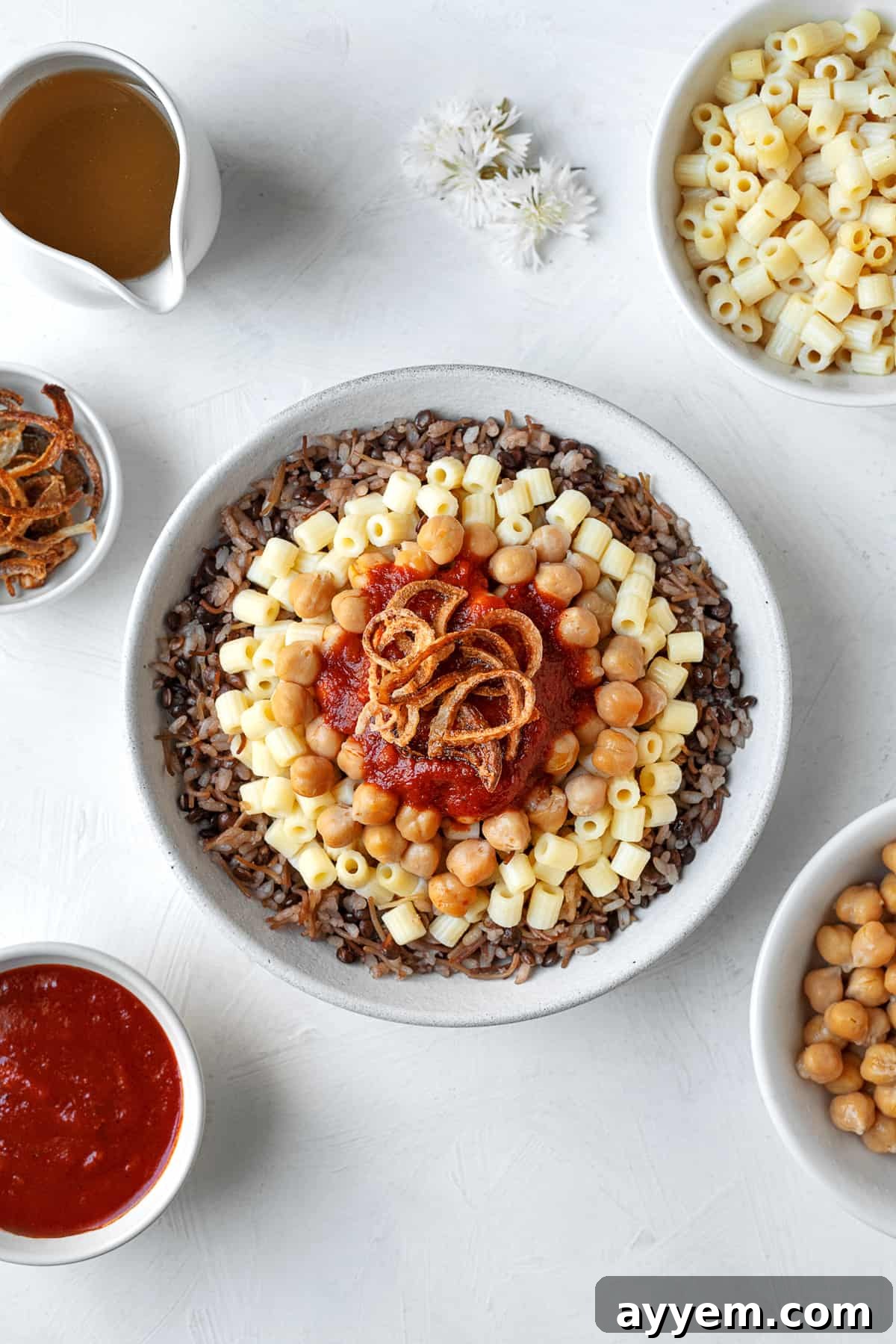 overhead image of a bowl of Egyptian koshari with rice, pasta, chickpeas, tomato sauce, and fried onions