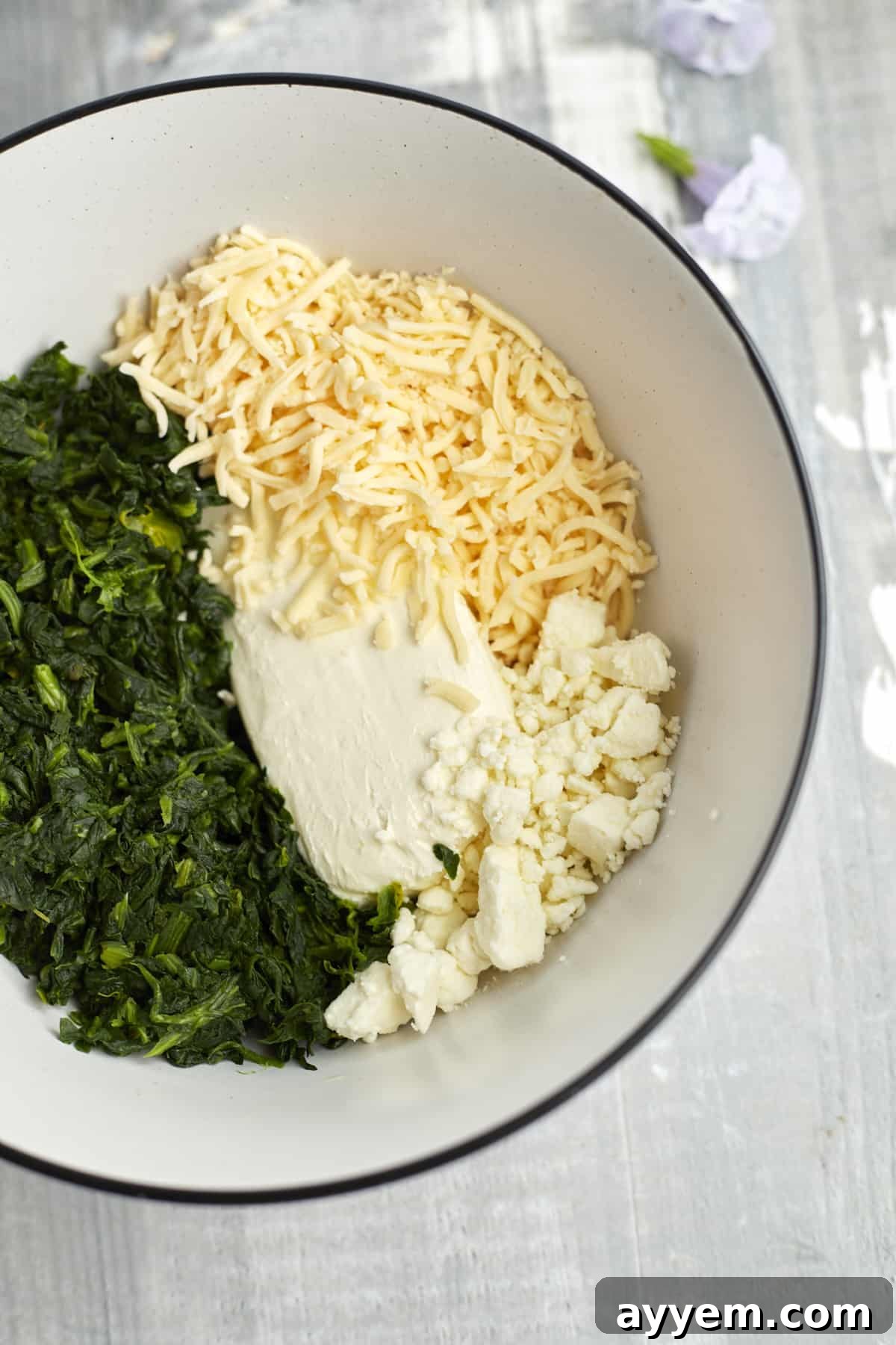 A bowl filled with cream cheese, crumbled feta, shredded mozzarella, and fresh spinach, ready to be mixed