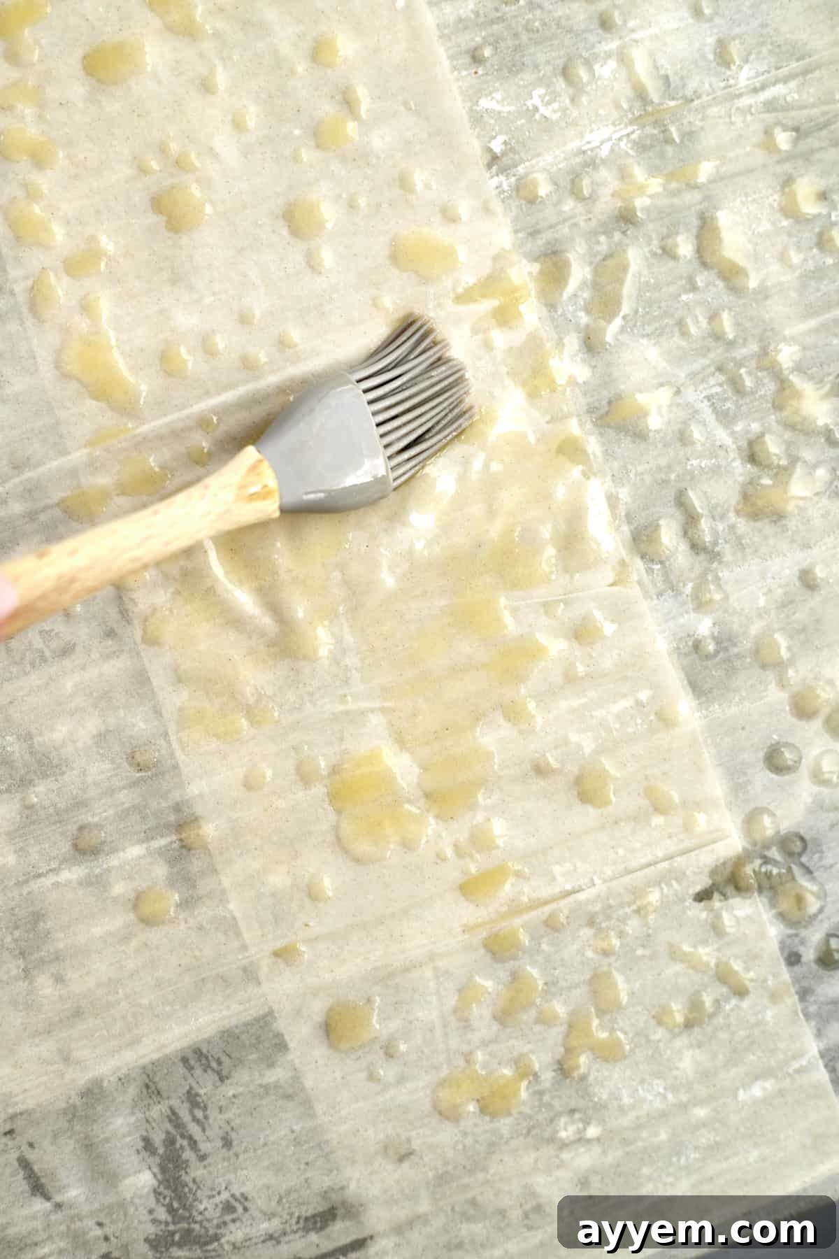 A skilled hand brushing melted butter onto a delicate sheet of phyllo dough in a baking dish