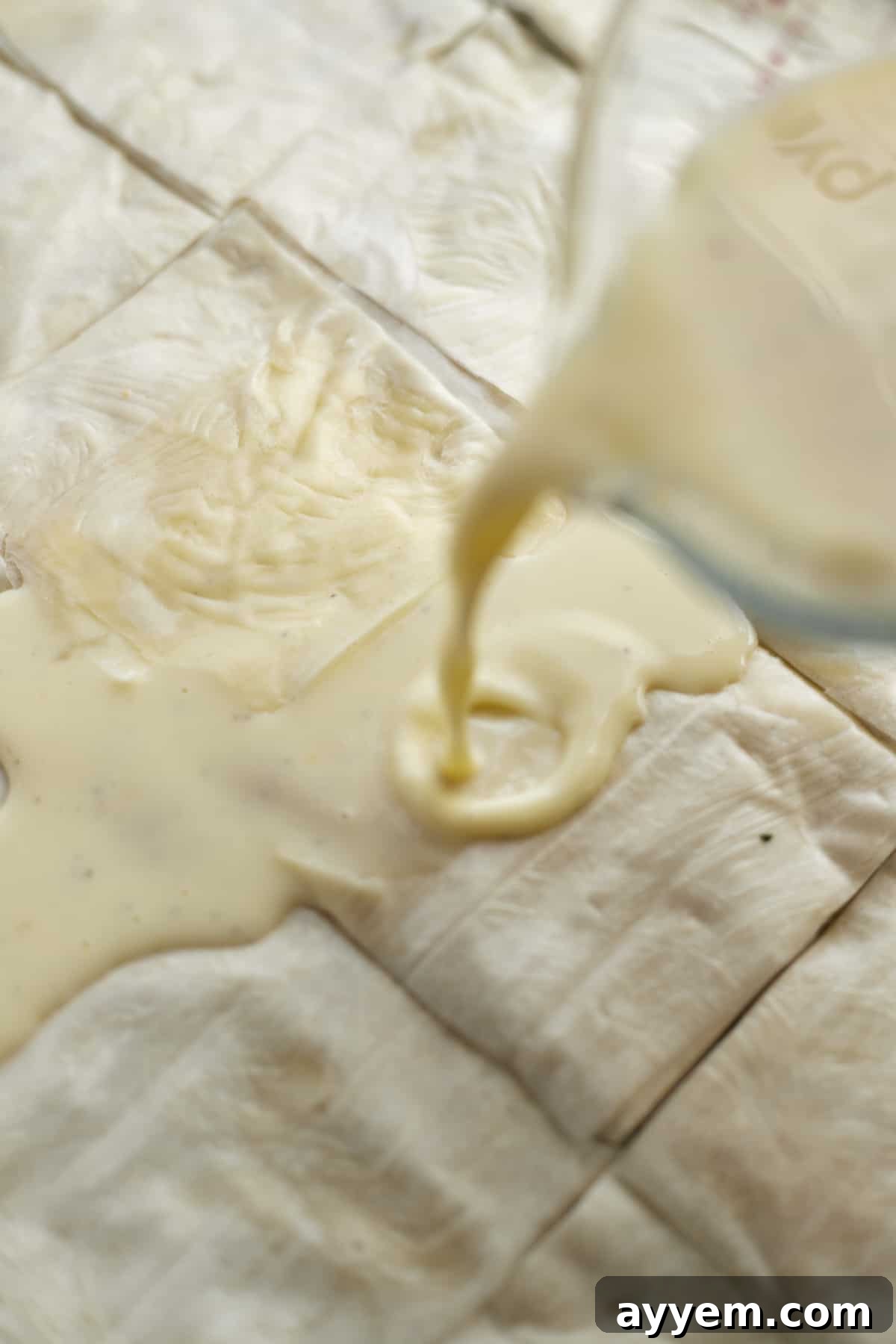 Unbaked phyllo spinach pie squares arranged in a baking dish, with an egg and milk mixture being poured over them