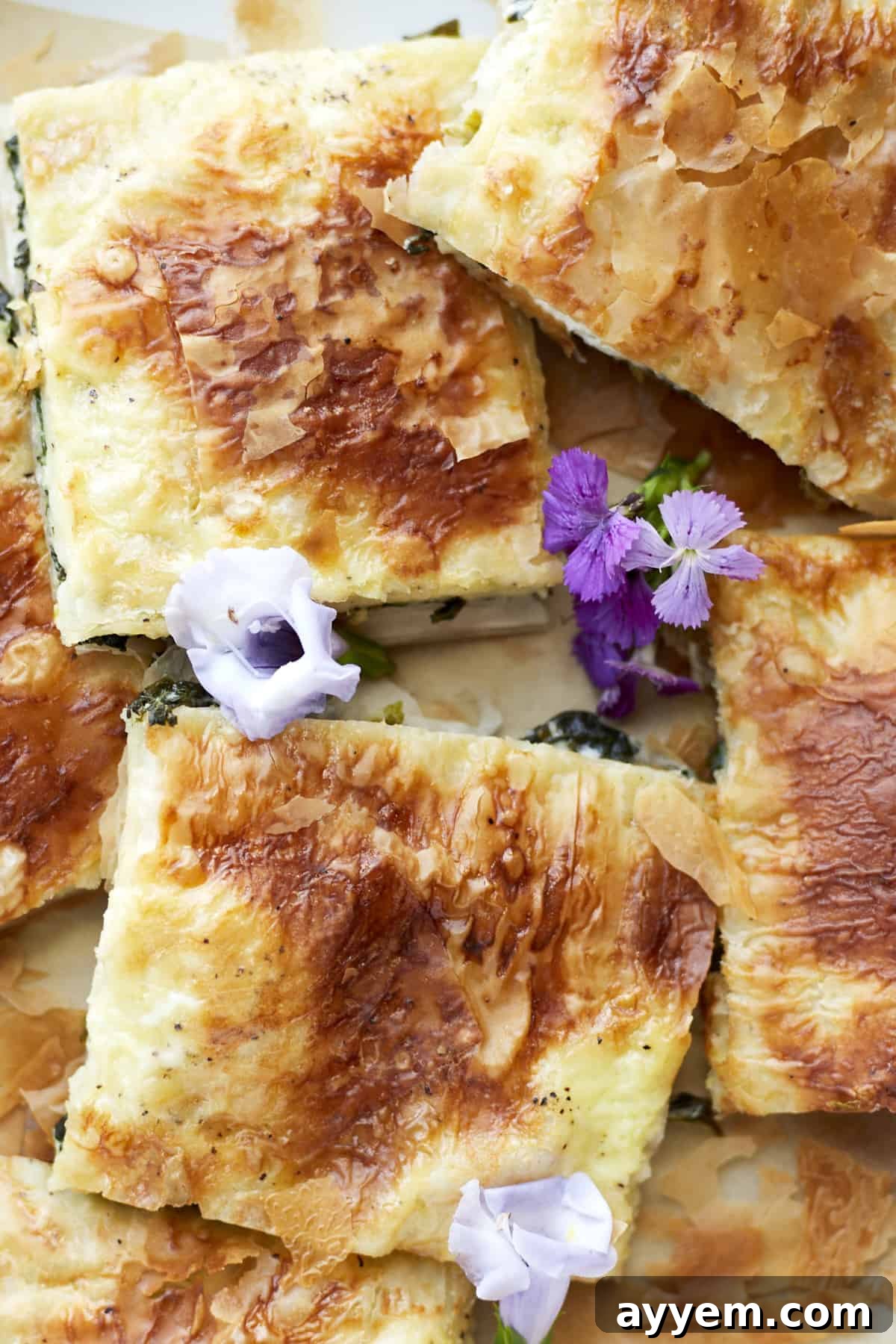 Freshly baked squares of phyllo spinach pie, golden and crispy, arranged in a serving dish