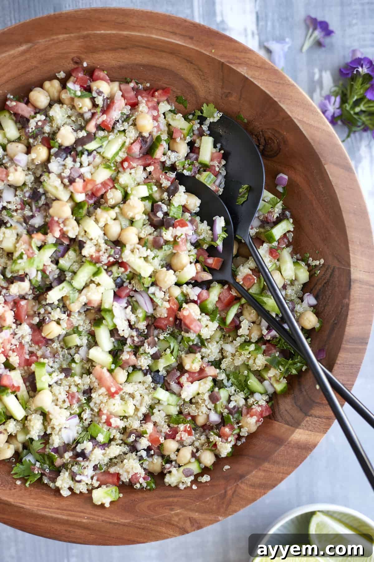 Mediterranean Quinoa Salad mixed up in a wooden bowl with serving spoons on the side