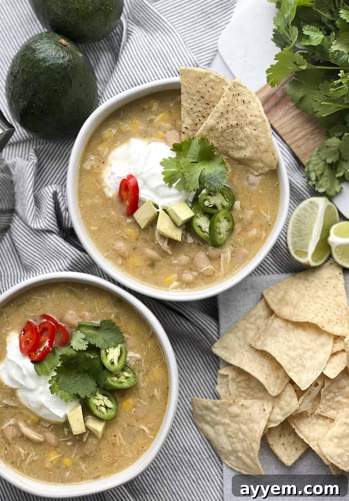 two bowls of white chicken chili with sour cream, avocado, jalapeño, and tortilla chips.