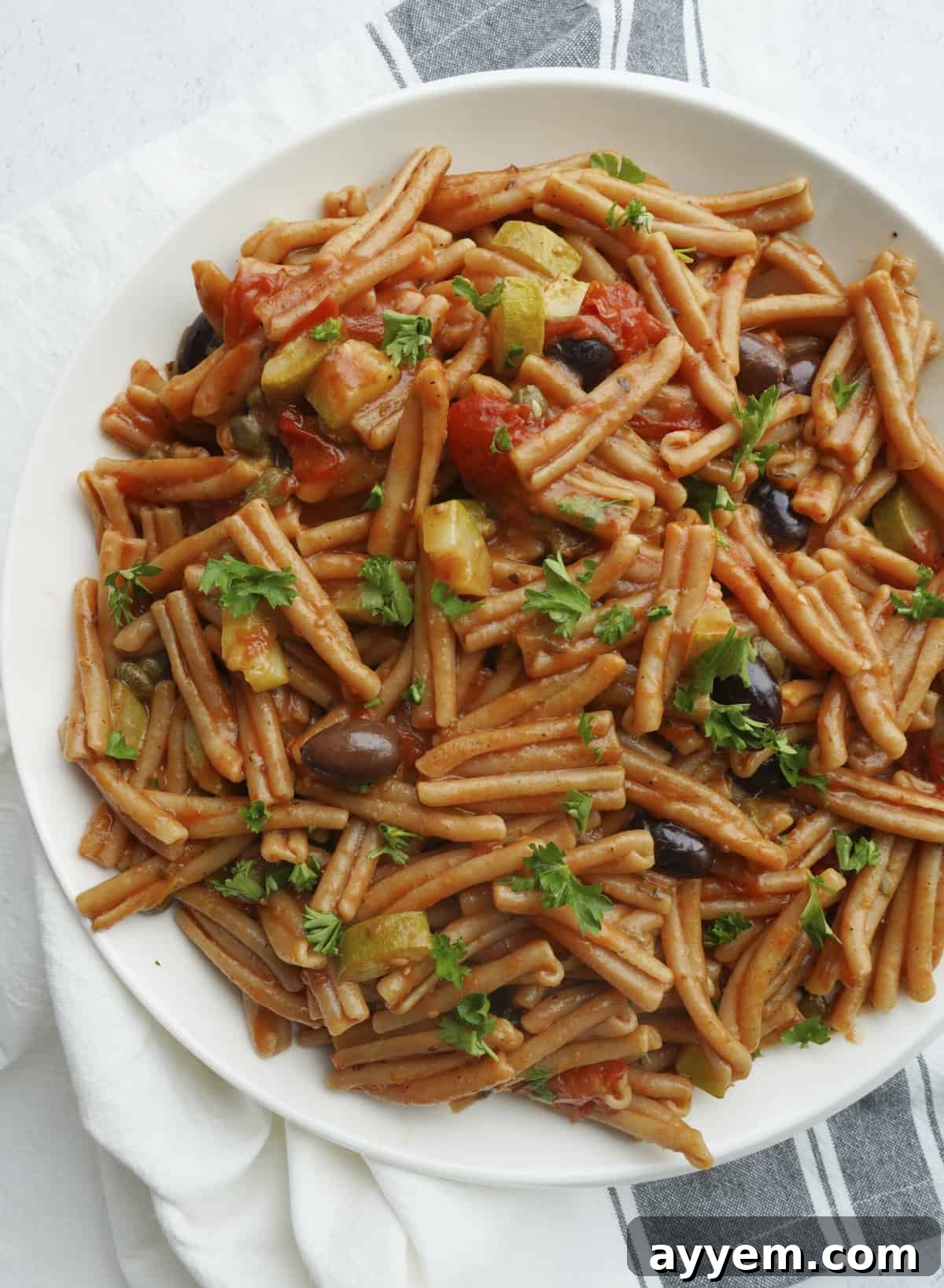 A vibrant bowl of one-pot pasta puttanesca made with whole wheat casarecce, showcasing tomatoes, olives, and capers.