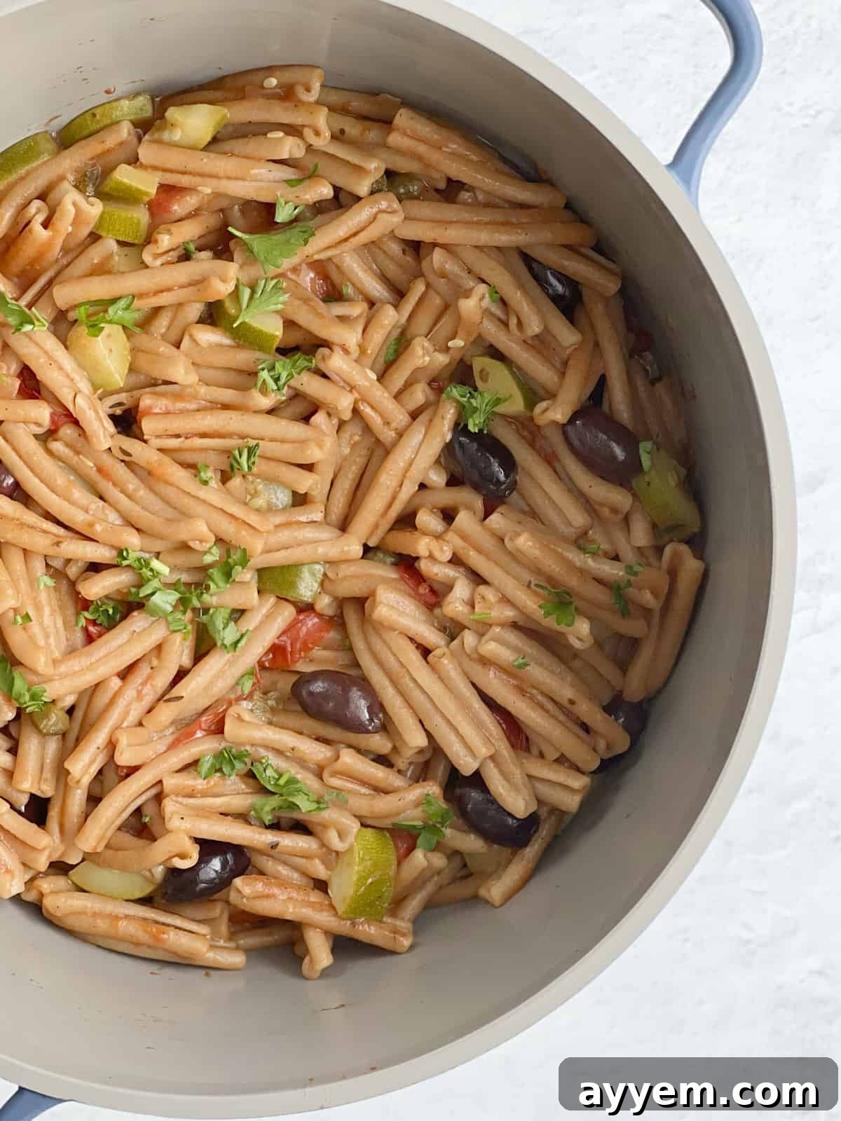 A deep pot filled with one-pot pasta puttanesca, featuring whole wheat pasta cooking in a rich, flavorful sauce.