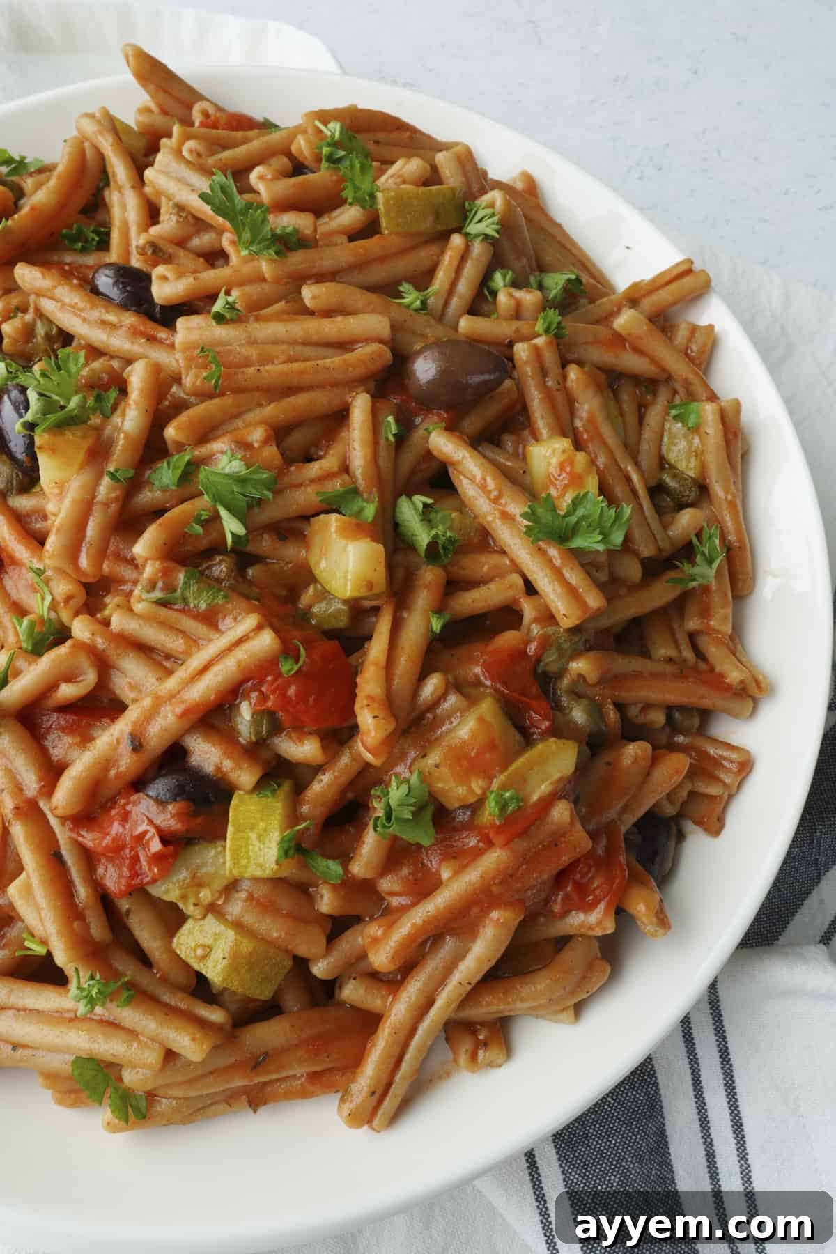 A close-up shot of a bowl of one-pot pasta puttanesca, highlighting the whole wheat casarecce pasta and the rich sauce.