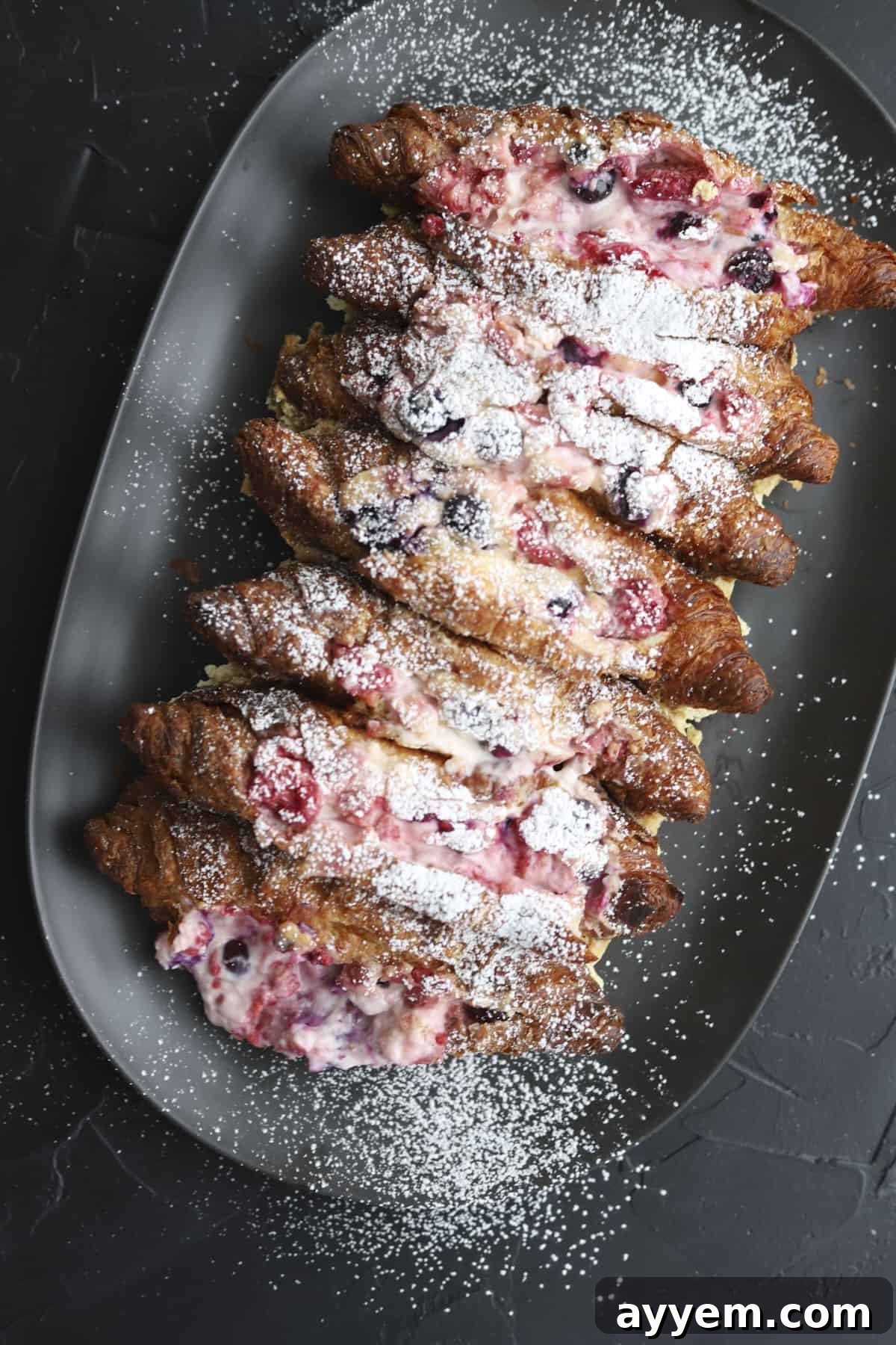A beautiful plate of Berry Stuffed Croissant French Toast, garnished with fresh berries and a dusting of powdered sugar.