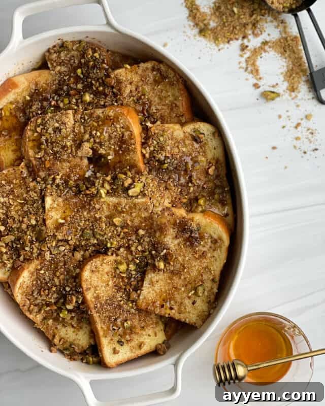 A close-up of a golden-brown Baklava French Toast casserole, glistening with syrup and topped with chopped pistachios and walnuts.