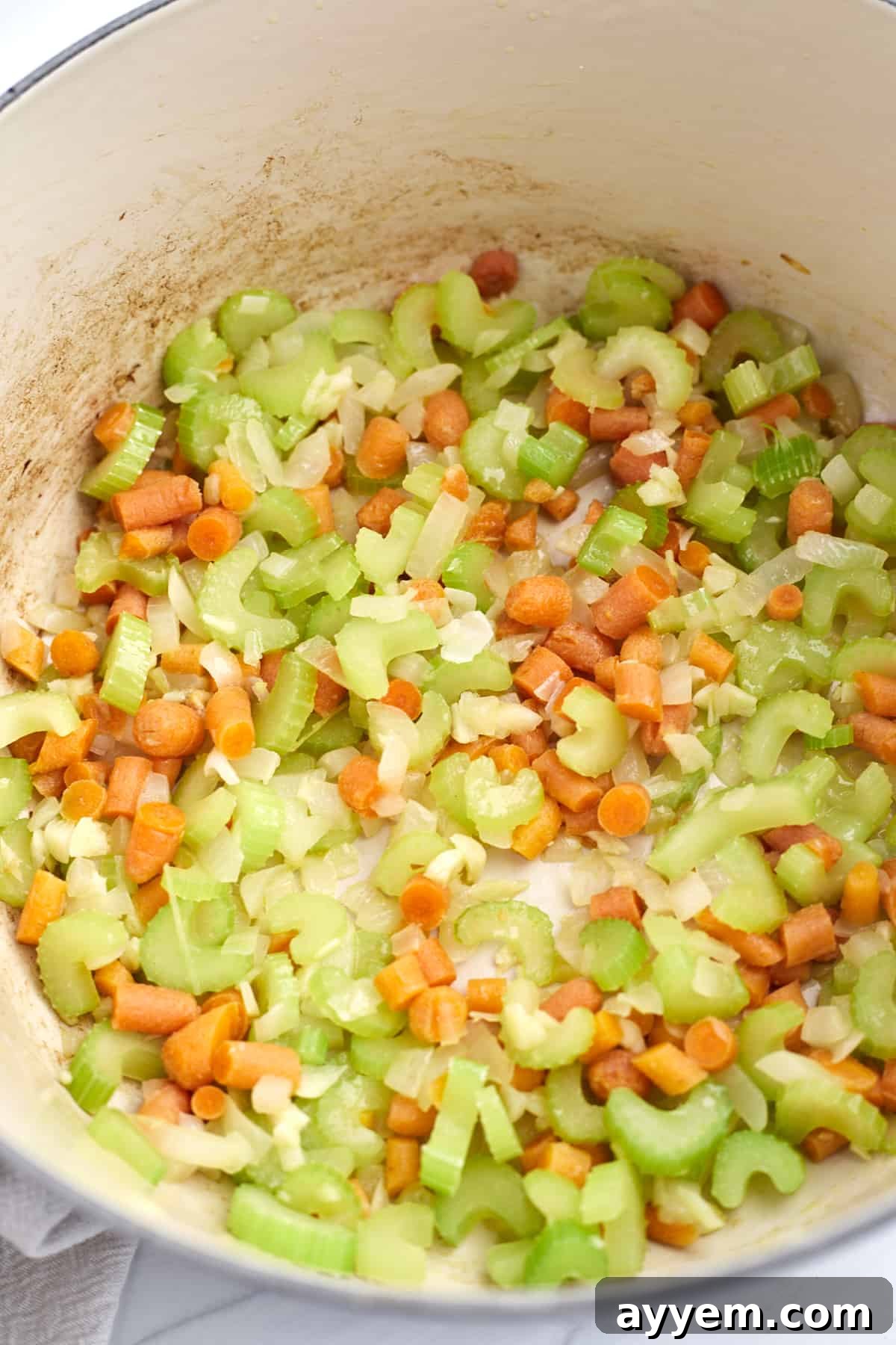 A close-up shot of a Dutch oven filled with a colorful medley of chopped celery, carrots, and onions, gently sautéing in olive oil. The steam rises softly, hinting at the aromatic flavors developing, a foundational step for a hearty soup.