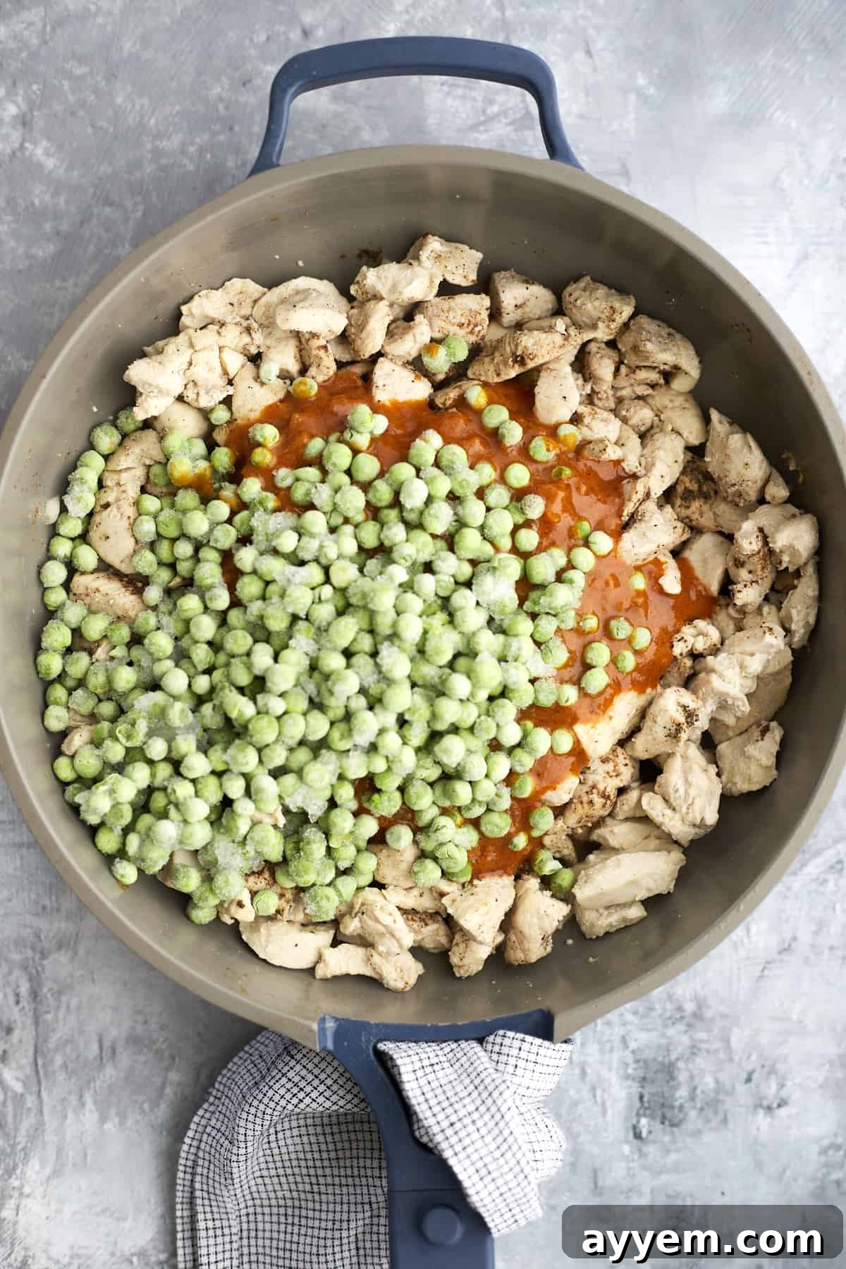 Chicken, curry sauce, and frozen peas simmering together in a skillet for Madras Curry.