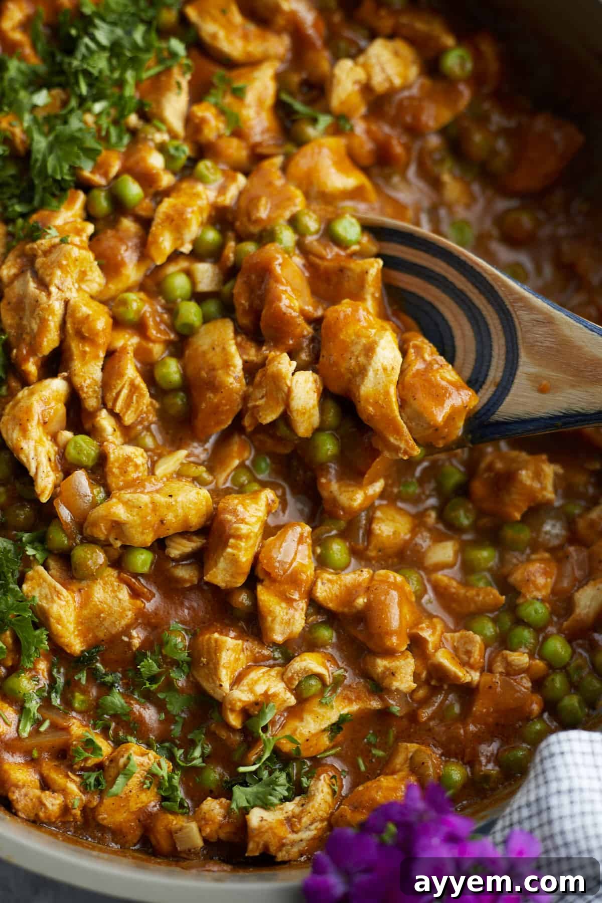 Close-up image of a wooden spoon stirring creamy Madras Curry Chicken in a deep pan.