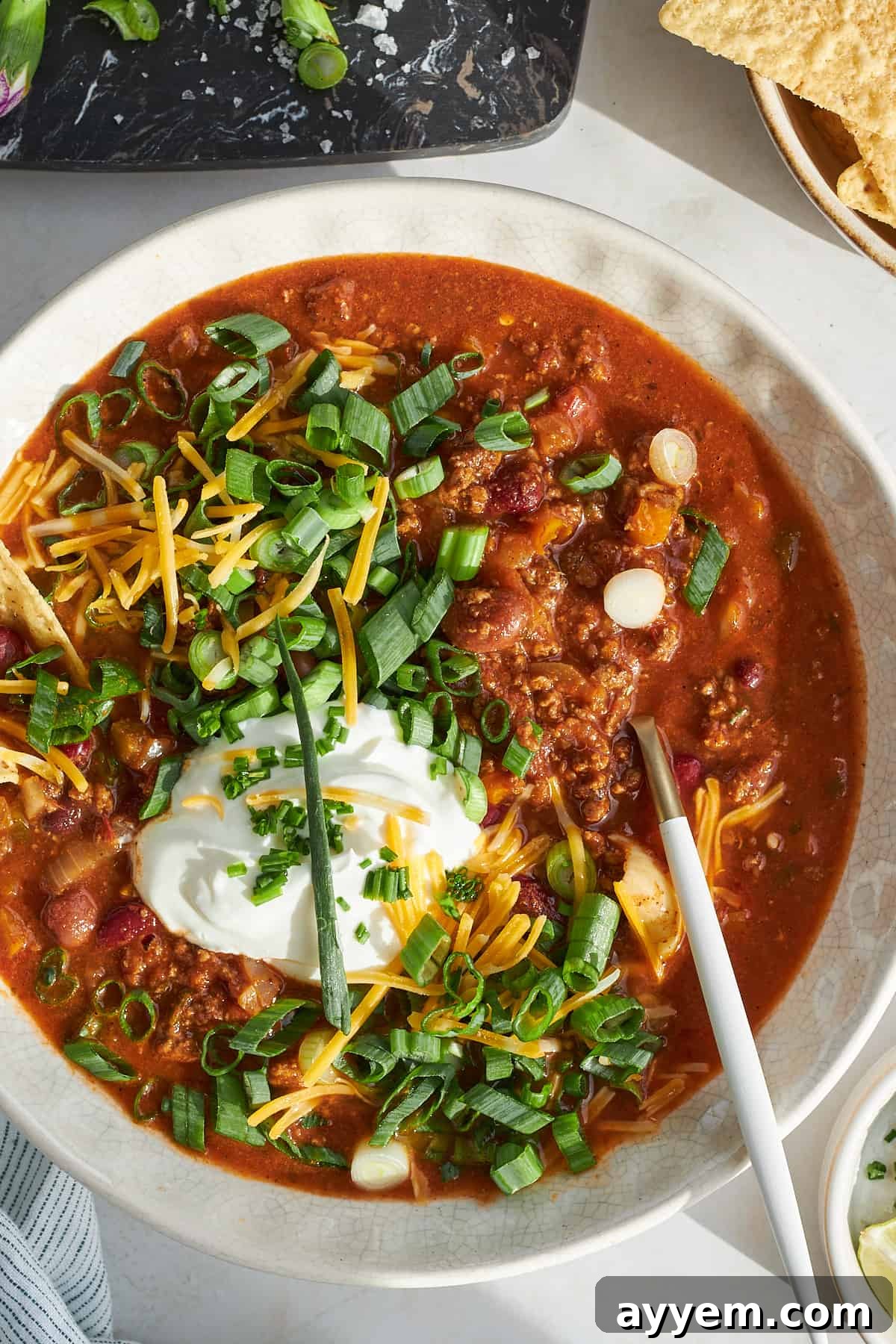 A close-up shot of a spoon lifting a rich, thick spoonful of slow cooker chili from a bowl, showcasing its hearty texture and ingredients.