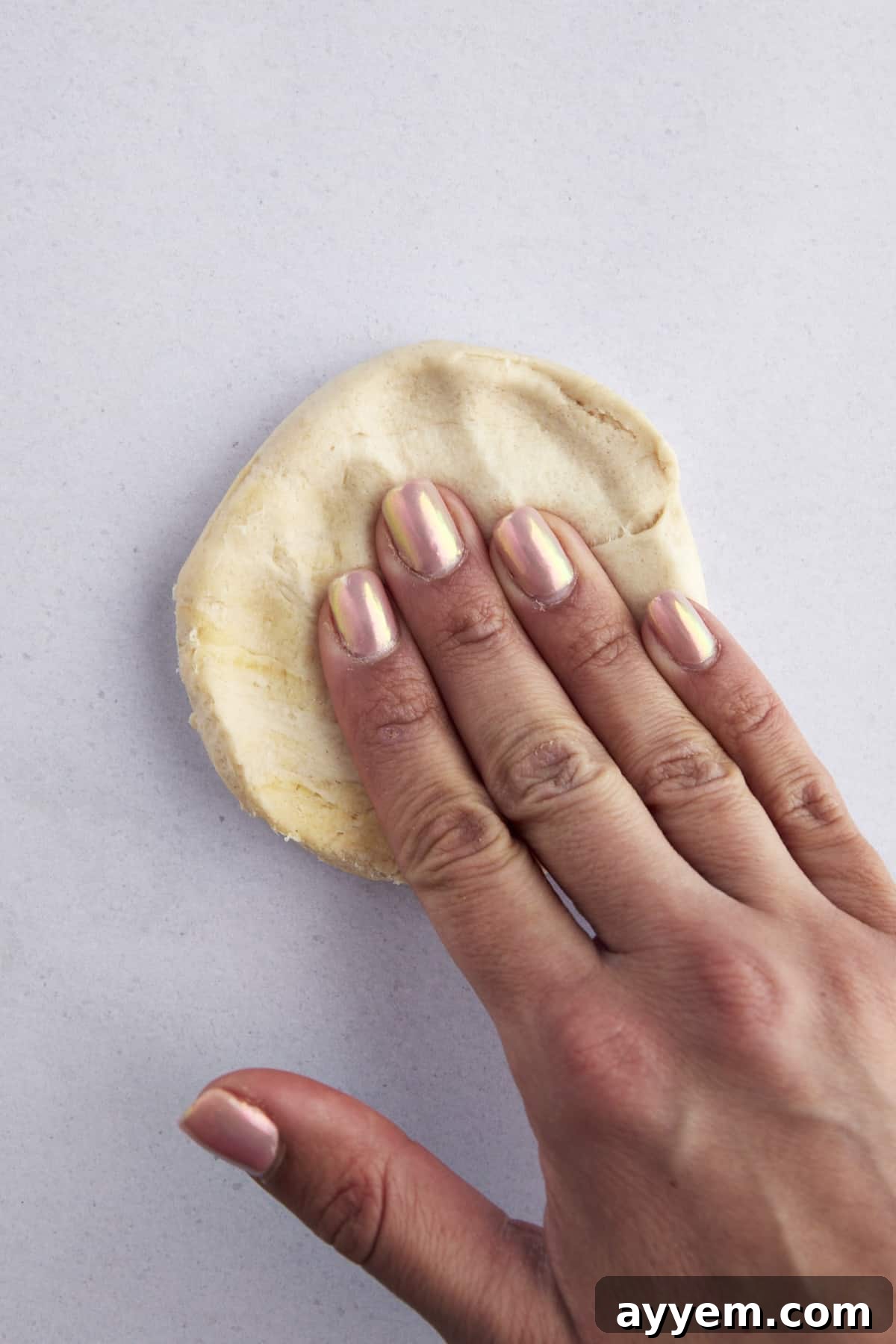Raw biscuit dough being flattened into a disc.