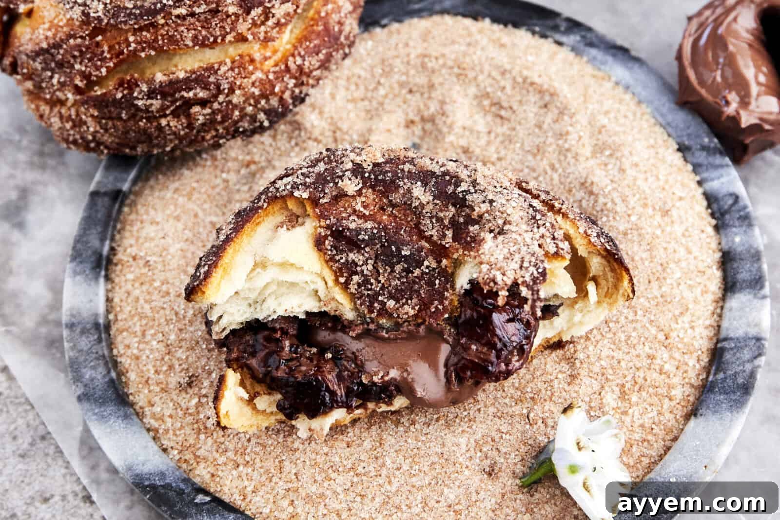 Half a Nutella stuffed biscuit doughnut in a bowl of cinnamon sugar.