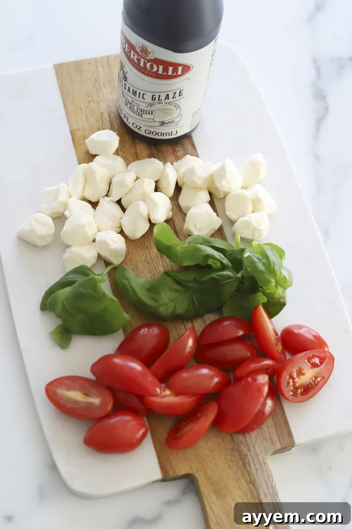 Overhead shot showcasing the fresh ingredients laid out for Caprese Avocado Toast preparation, including ripe avocados, sliced sourdough bread, fresh mozzarella pearls, halved grape tomatoes, a bottle of balsamic glaze, fresh basil leaves, and salt and pepper.