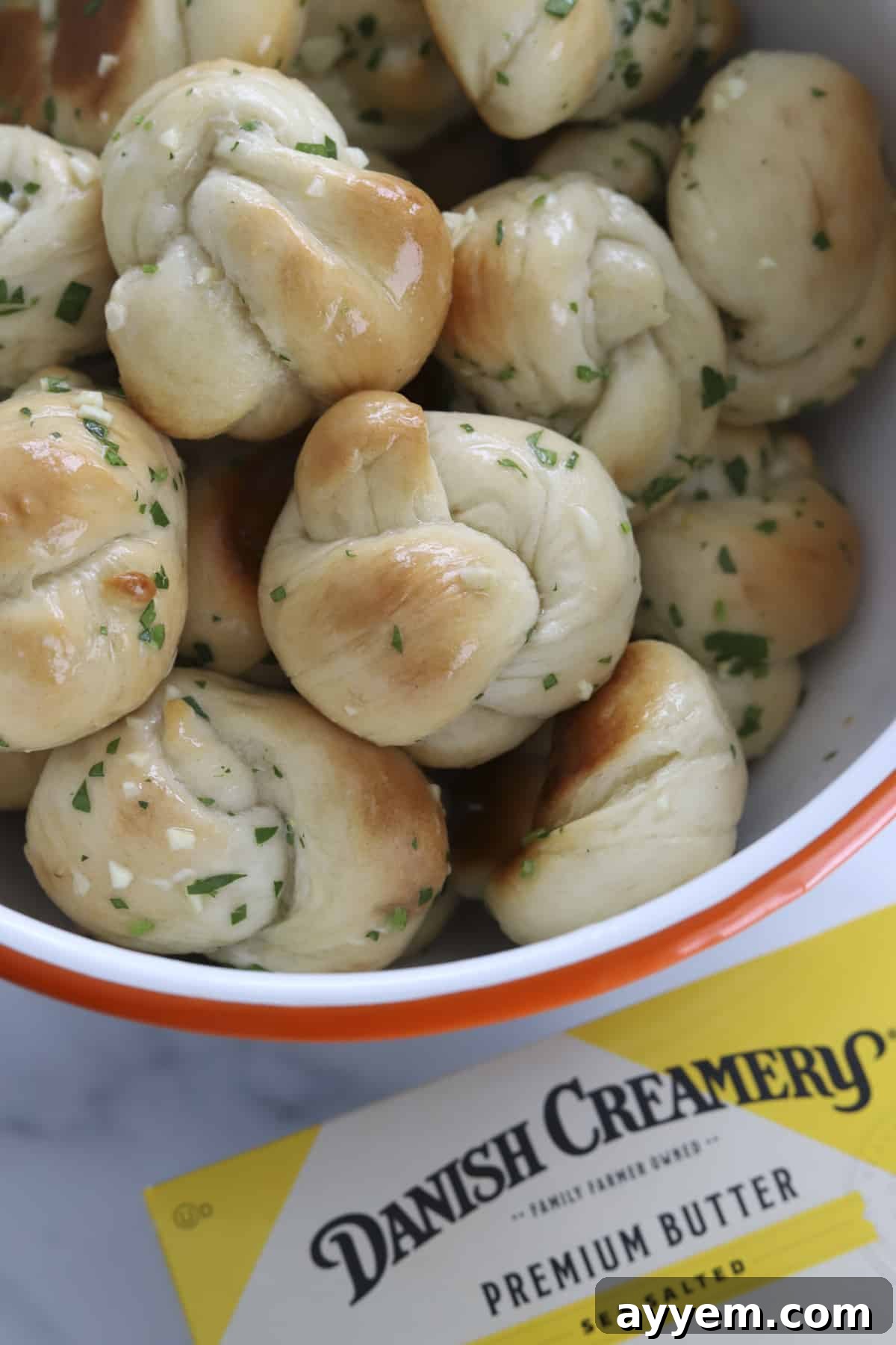 Freshly baked cheesy garlic knots served in a rustic bowl, glistening with butter and herbs, ready for serving.