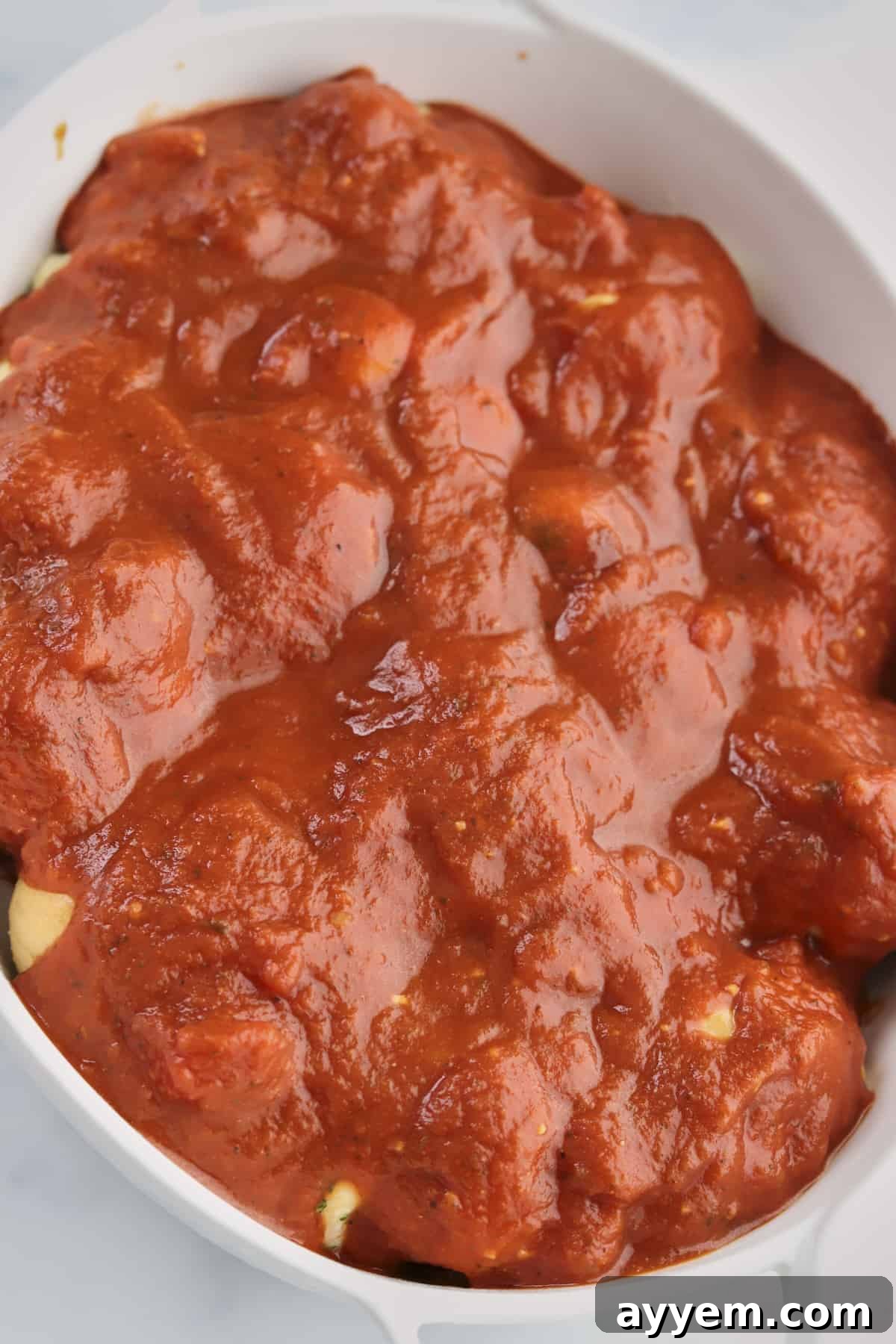 Garlic knots generously topped with vibrant marinara sauce, preparing for the final layer of cheese.
