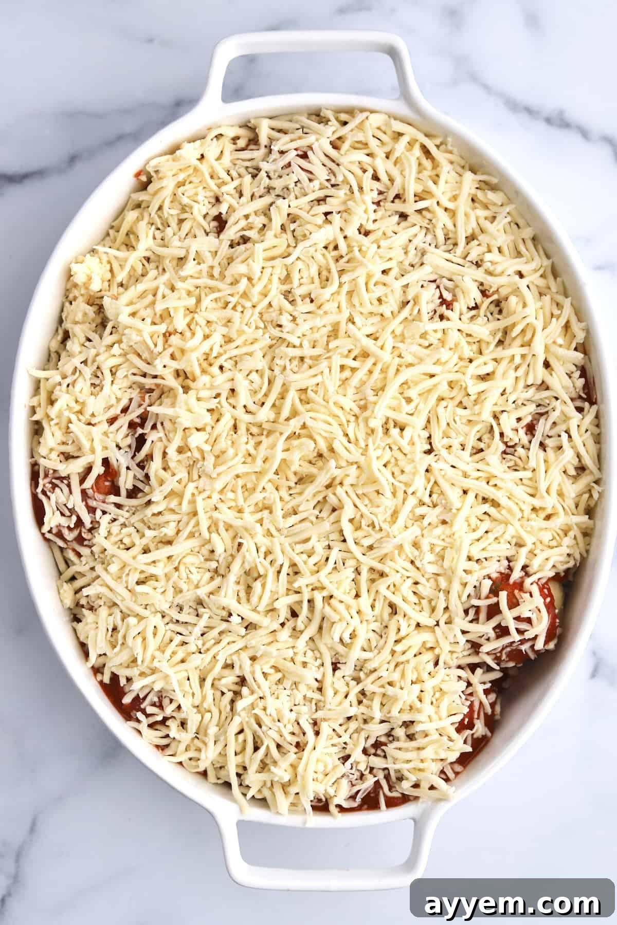 The final stage before baking: garlic knots smothered in marinara and a generous amount of shredded mozzarella cheese.