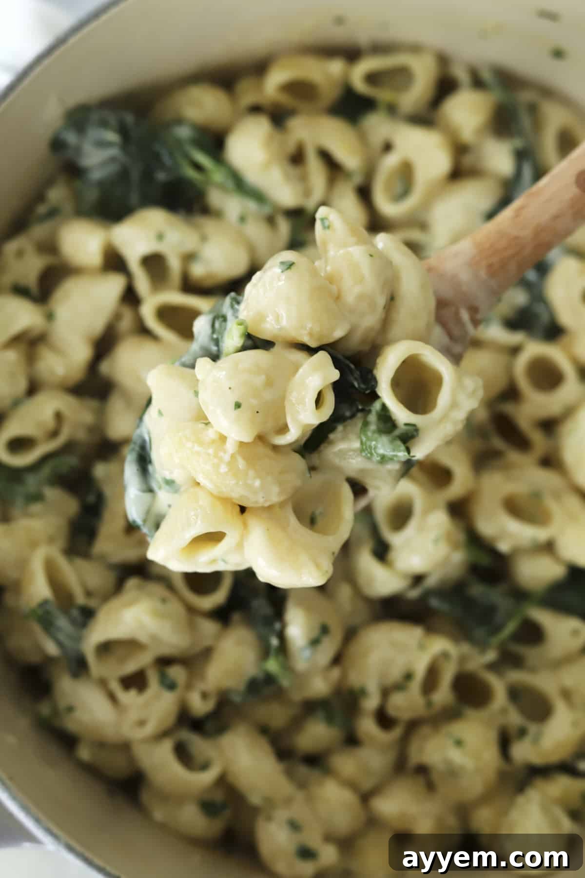 A spoon lifting a scoop of creamy lemon garlic pasta from a pot, garnished with fresh herbs.