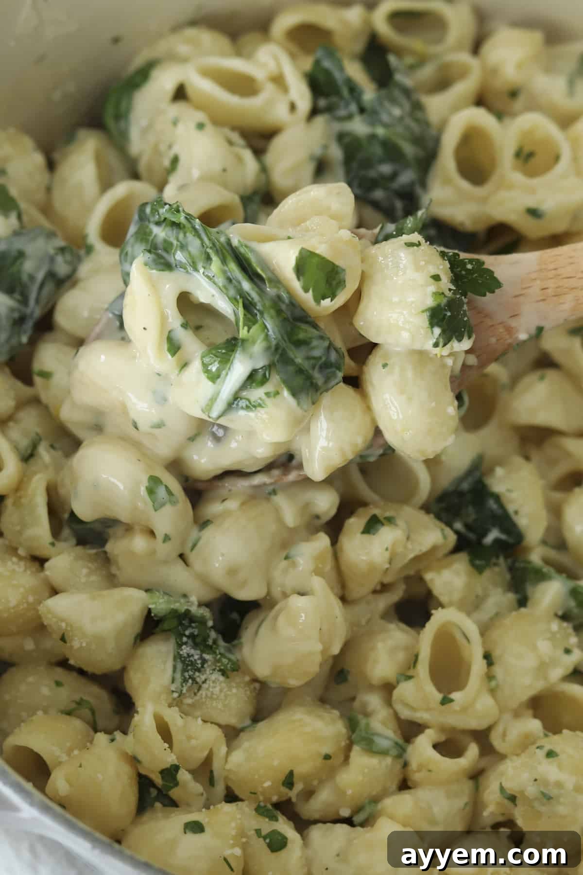 Close-up overhead image of lemon garlic pasta on a wooden spoon, highlighting the creamy texture and fresh spinach.