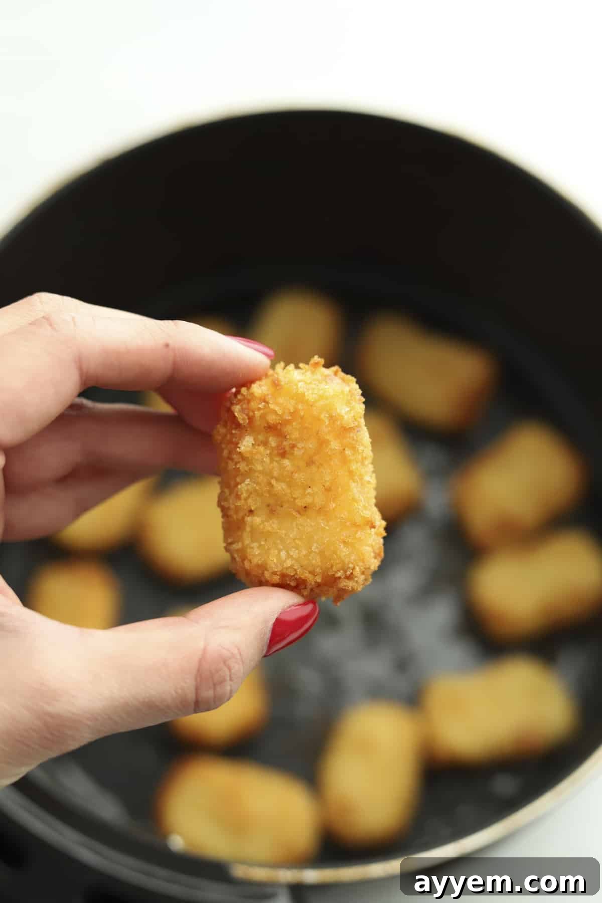 Hand holding an air fryer potato nugget, showcasing its golden-brown crispiness.