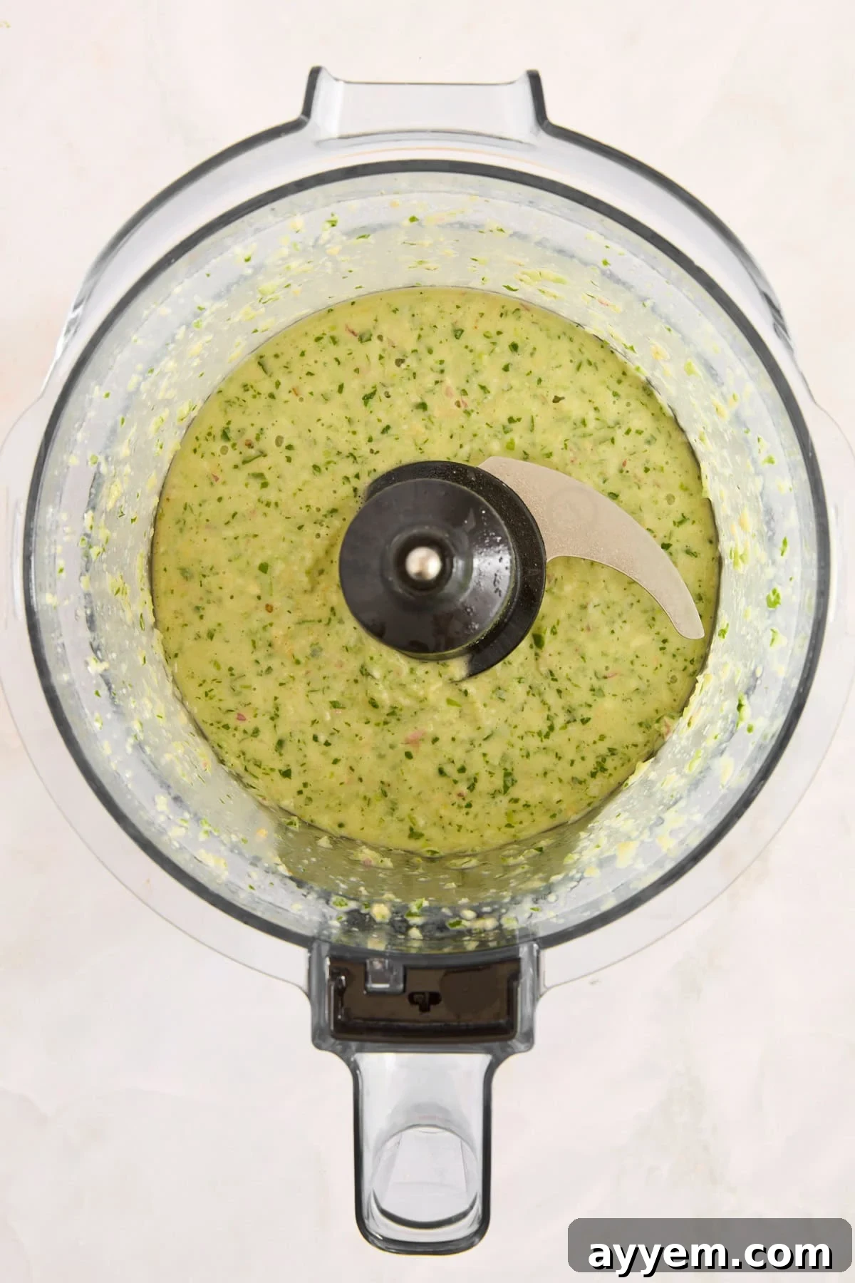 Green goddess dressing blending in a food processor, turning into a smooth sauce.