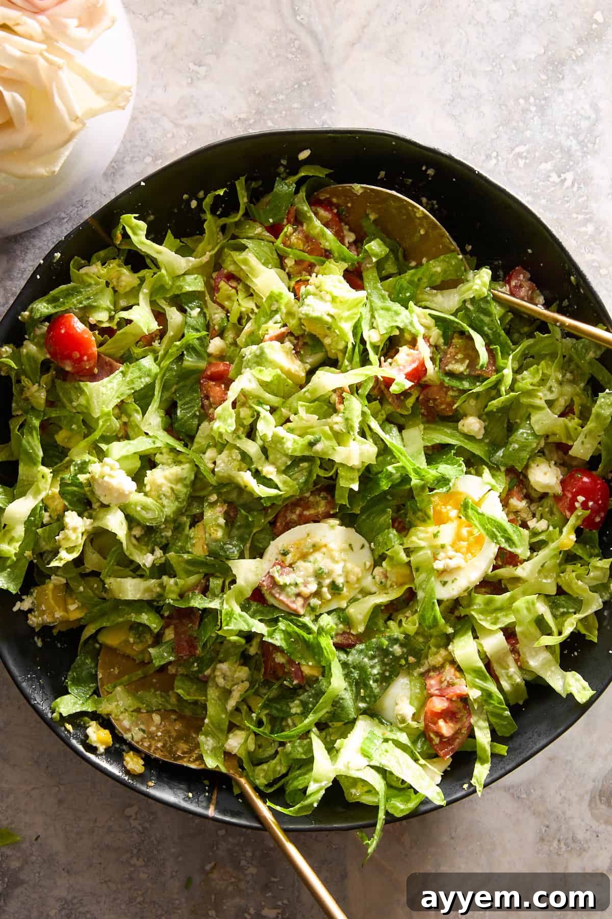 A Cobb salad being tossed with green goddess dressing, showing fresh ingredients.