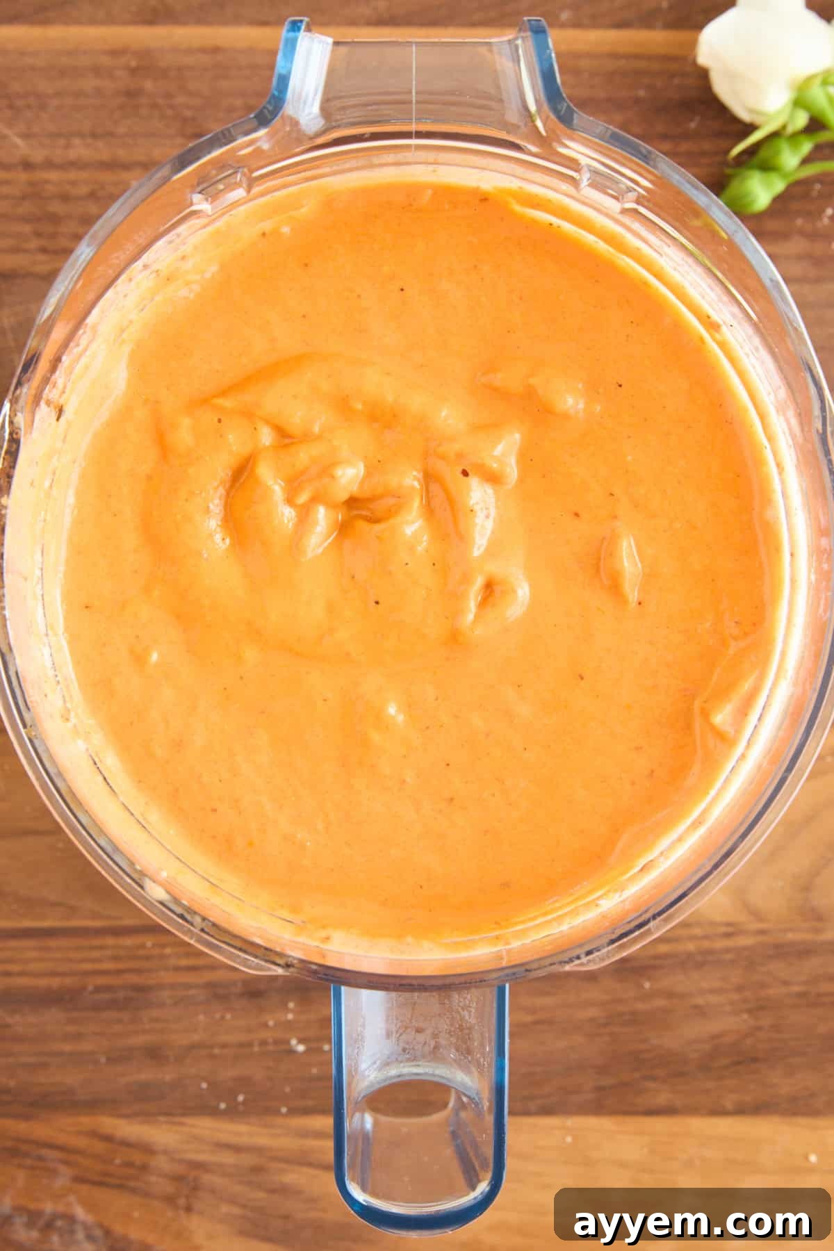 A blender filled with a vibrant orange, creamy roasted red pepper and cauliflower soup, partially blended, ready for serving. The setting is clean and inviting.