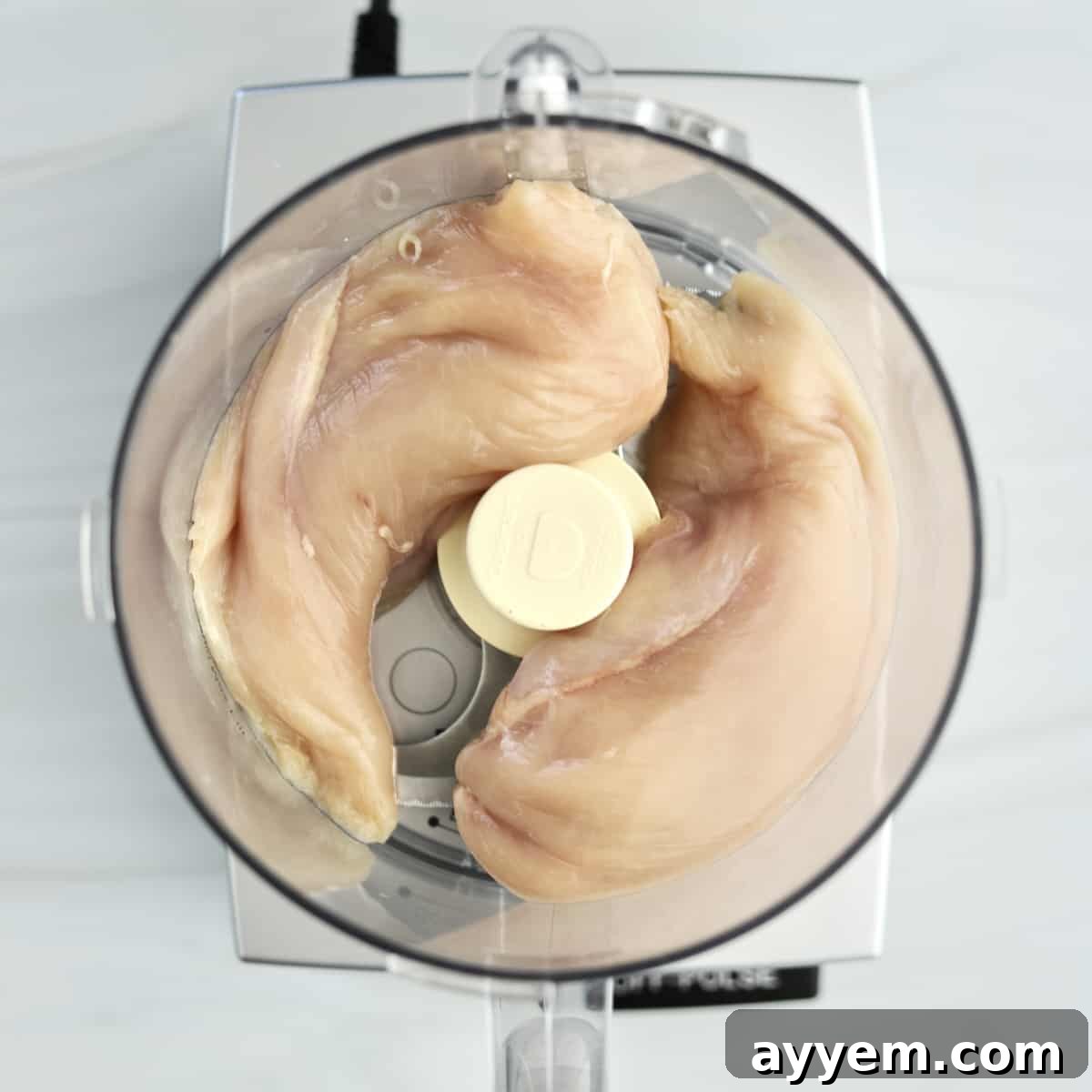 overhead image of raw chicken breasts in a food processor.