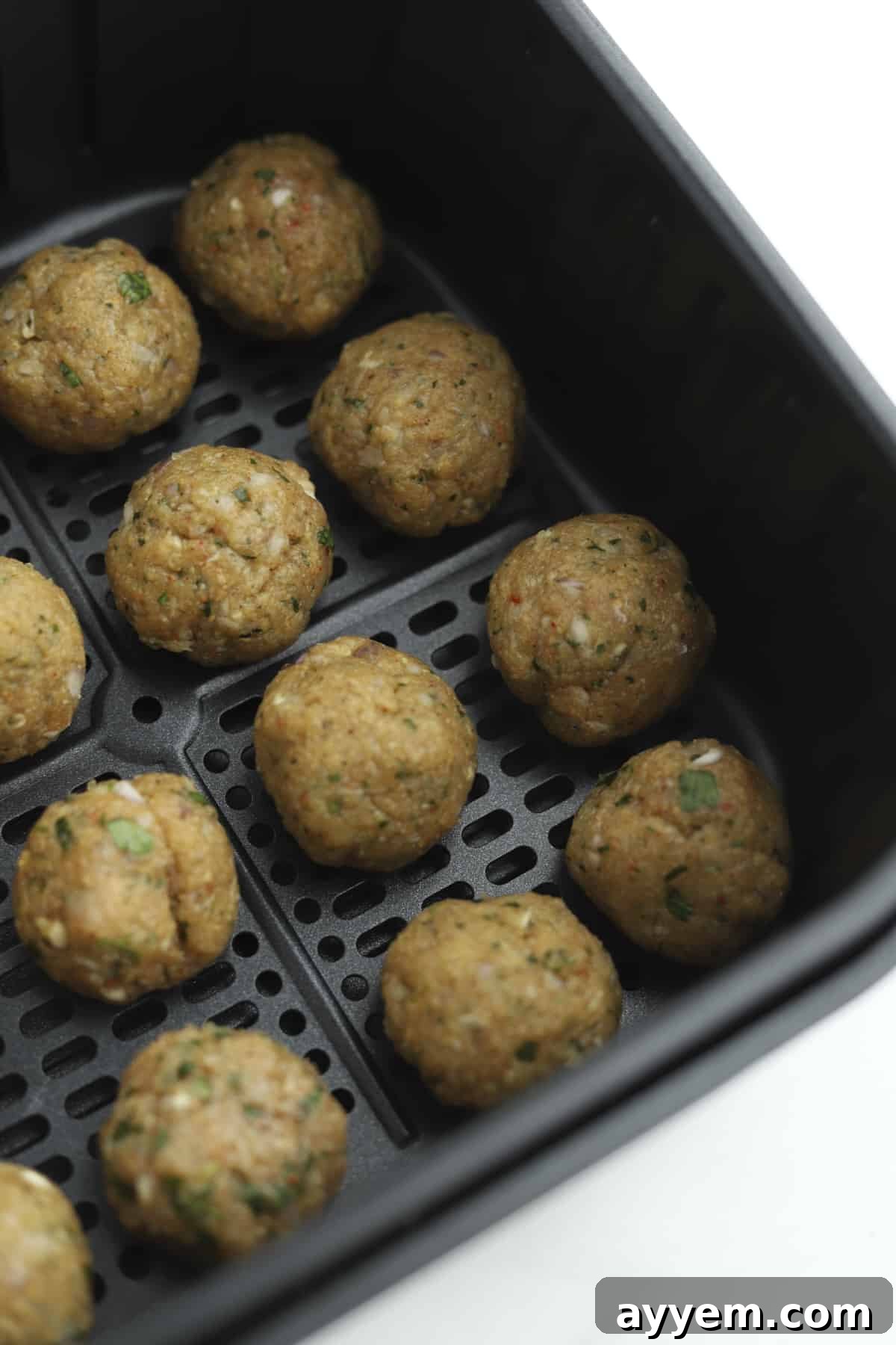 Raw chicken kofta meatballs in an air fryer basket. 