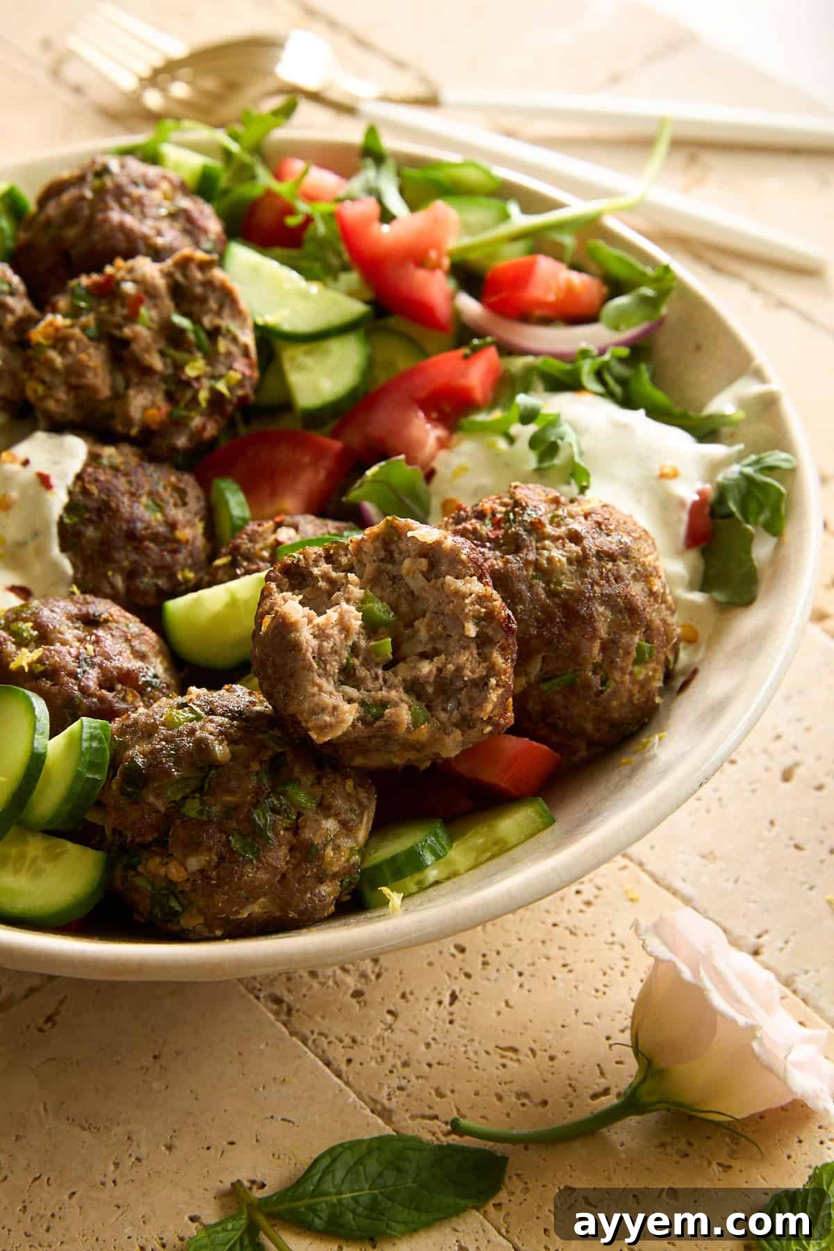 A refreshing plate of cucumber and tomato salad, elegantly topped with tender beef kofta meatballs and a dollop of creamy tzatziki, ready to serve as a complete, fresh meal.