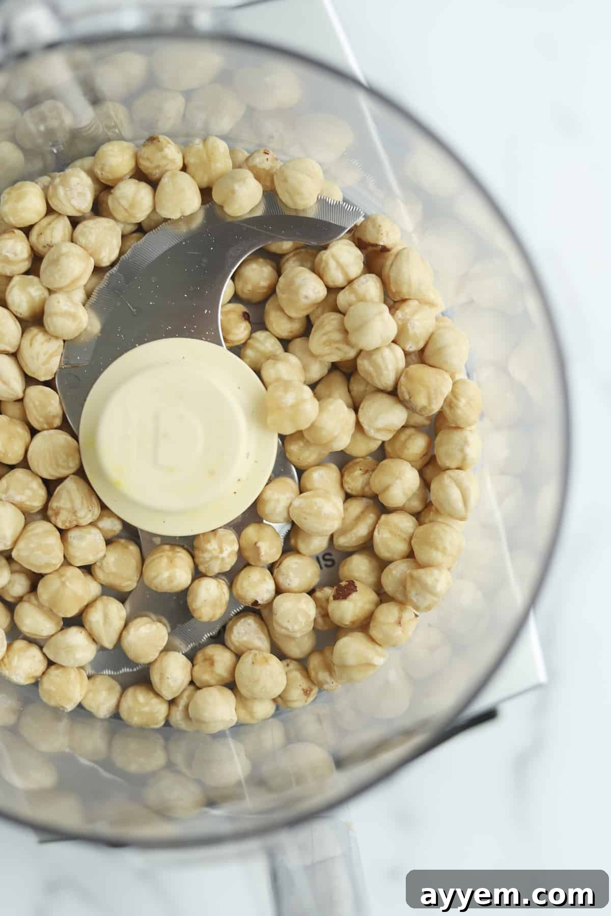 Close-up of roasted hazelnuts in a food processor, ready to be transformed into butter.