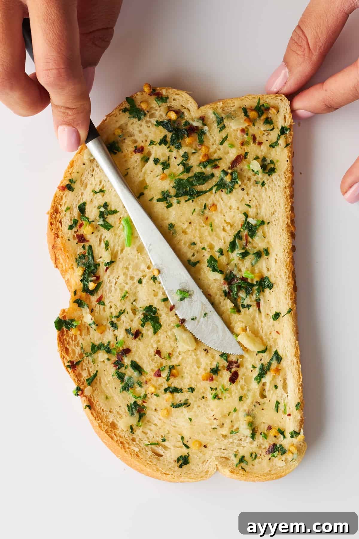 A knife spreading the fragrant herbed garlic butter evenly over a thick slice of bread.