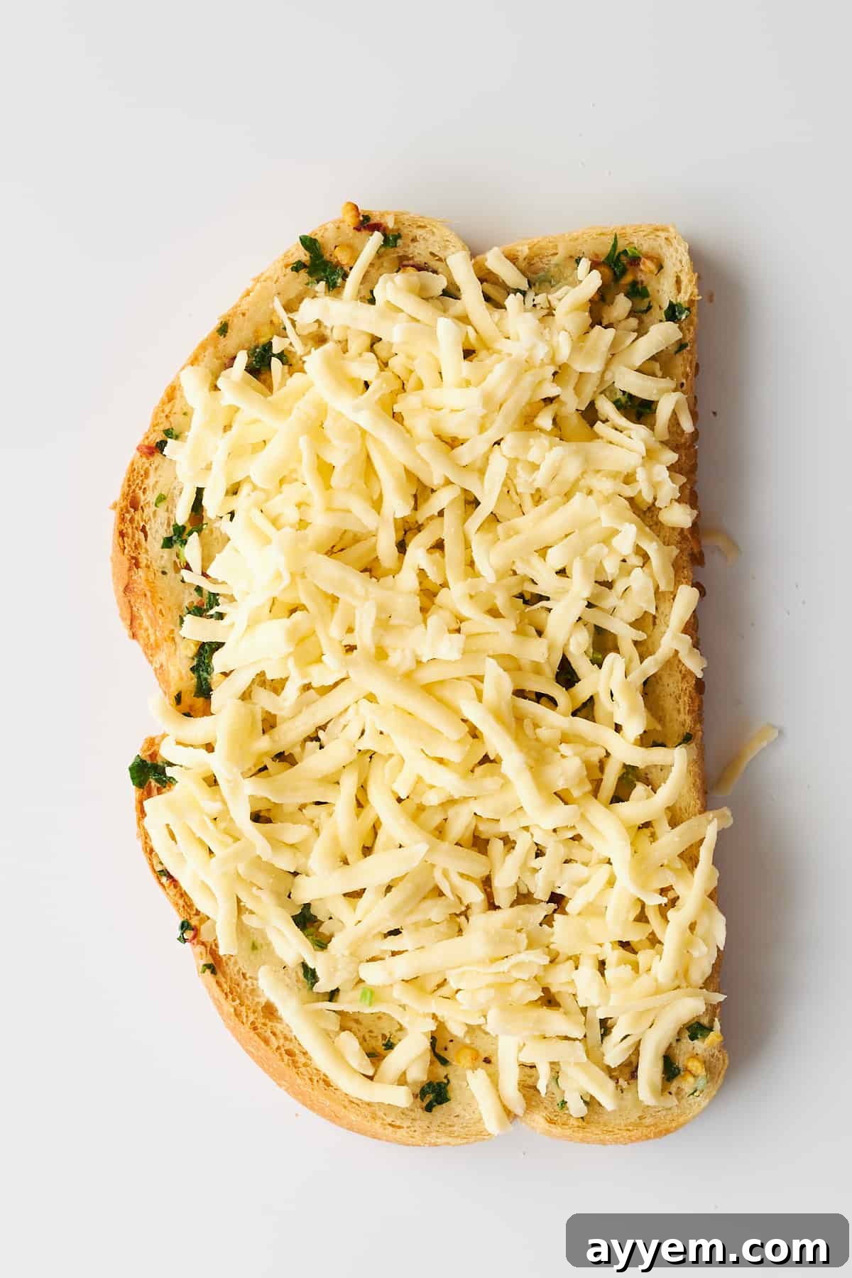 A slice of bread topped with a generous layer of herbed butter and sprinkled with mozzarella cheese, ready for the air fryer.