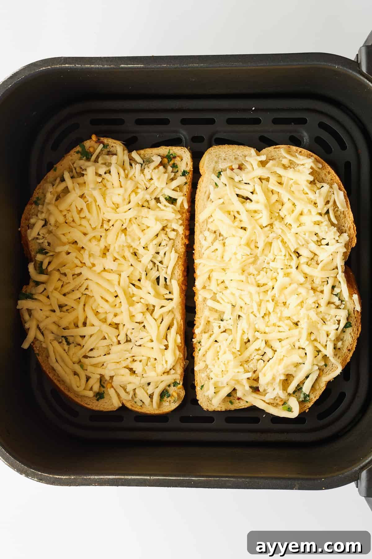 Two pieces of cheesy garlic toast, glistening with melted cheese, nestled perfectly in an air fryer basket, halfway through cooking.