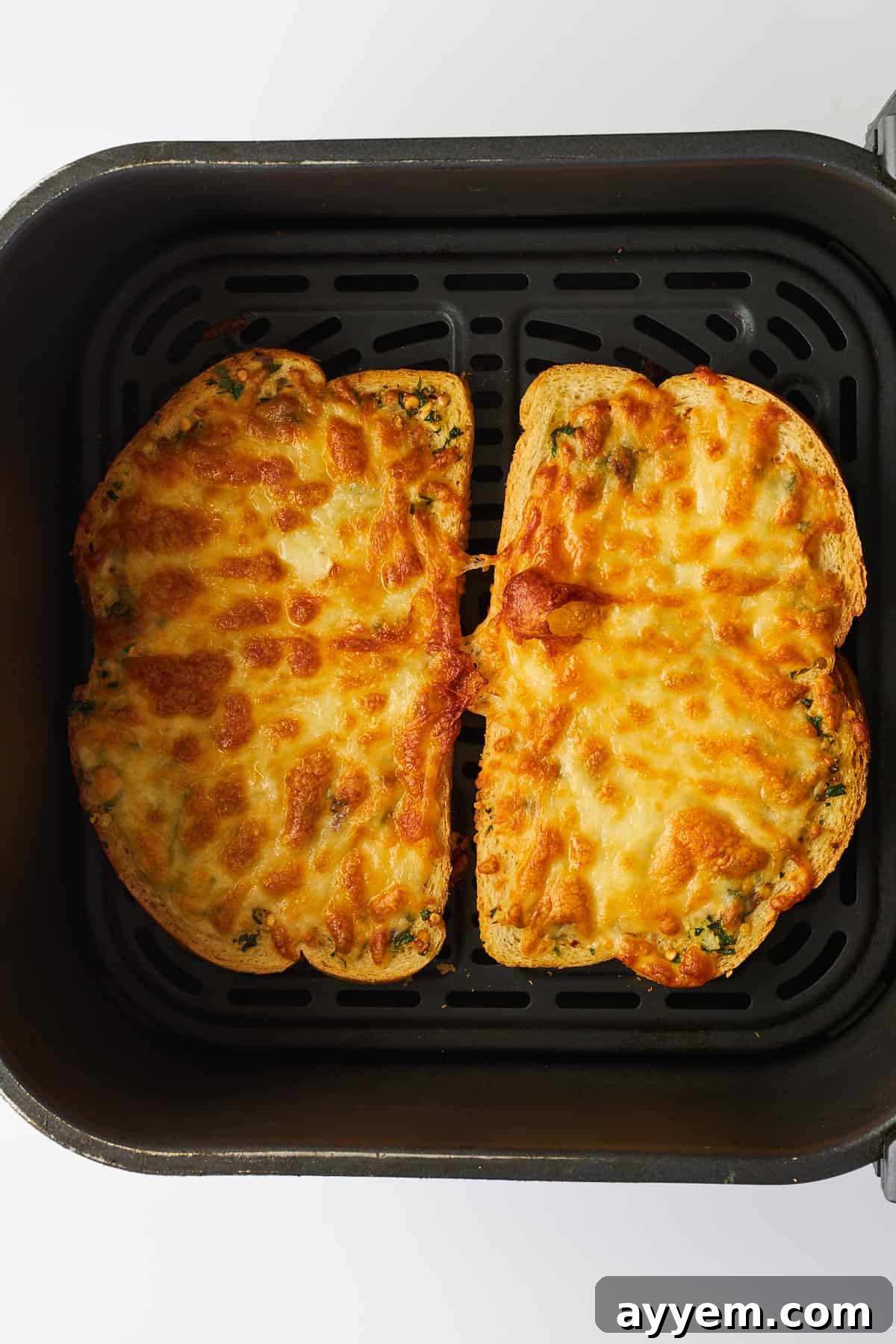 Two finished slices of crispy, golden-brown cheesy garlic toast, hot and ready to eat, resting in the air fryer basket after cooking.