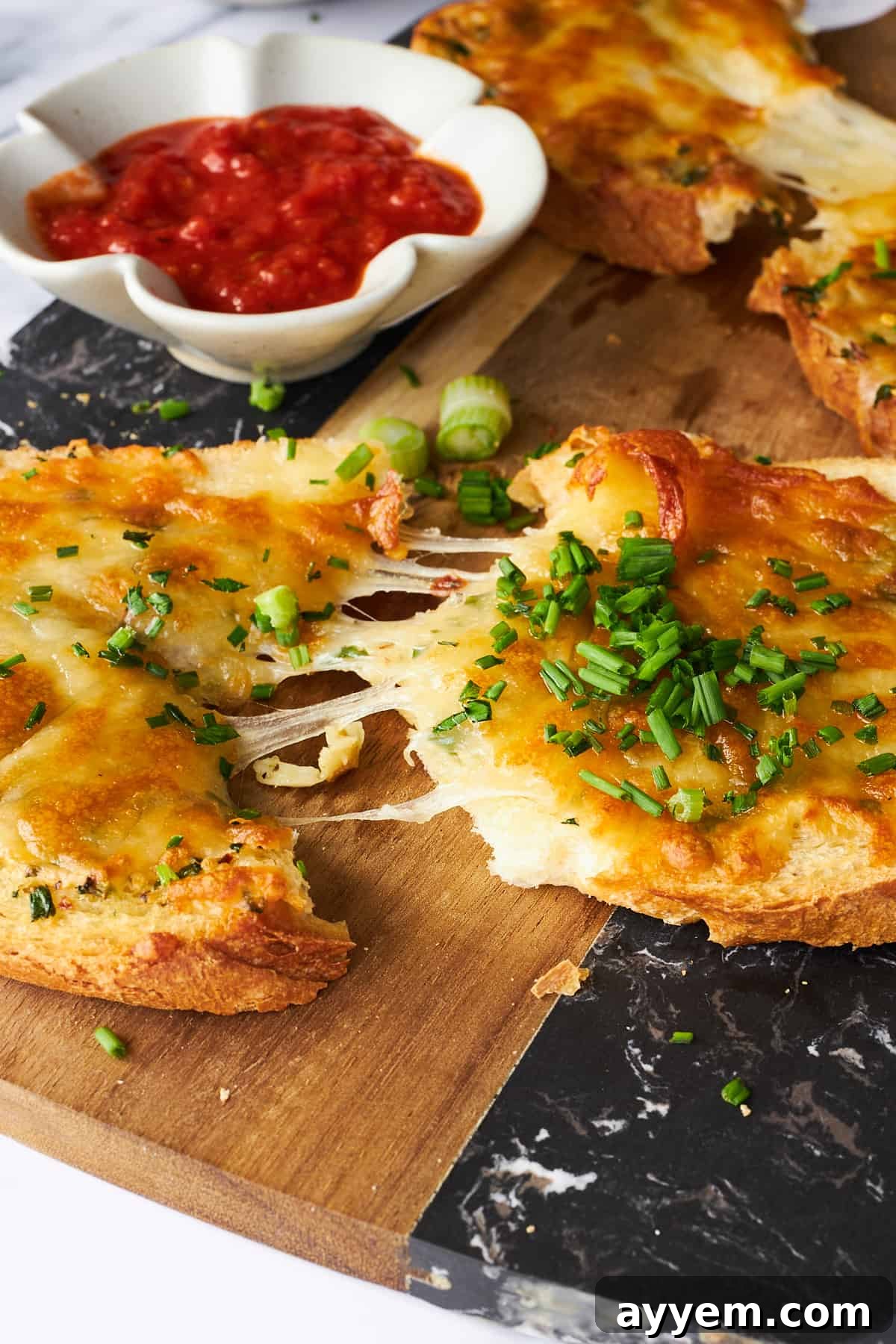 A hand pulling apart a slice of hot, stringy cheesy garlic toast, showcasing the gooey melted mozzarella and crispy bread.